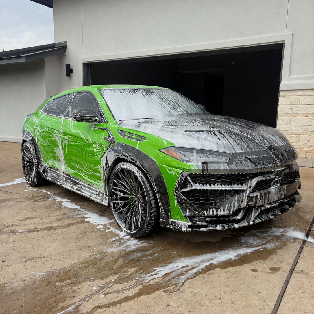 Green sports car being washed with soap and foam outside of a house.