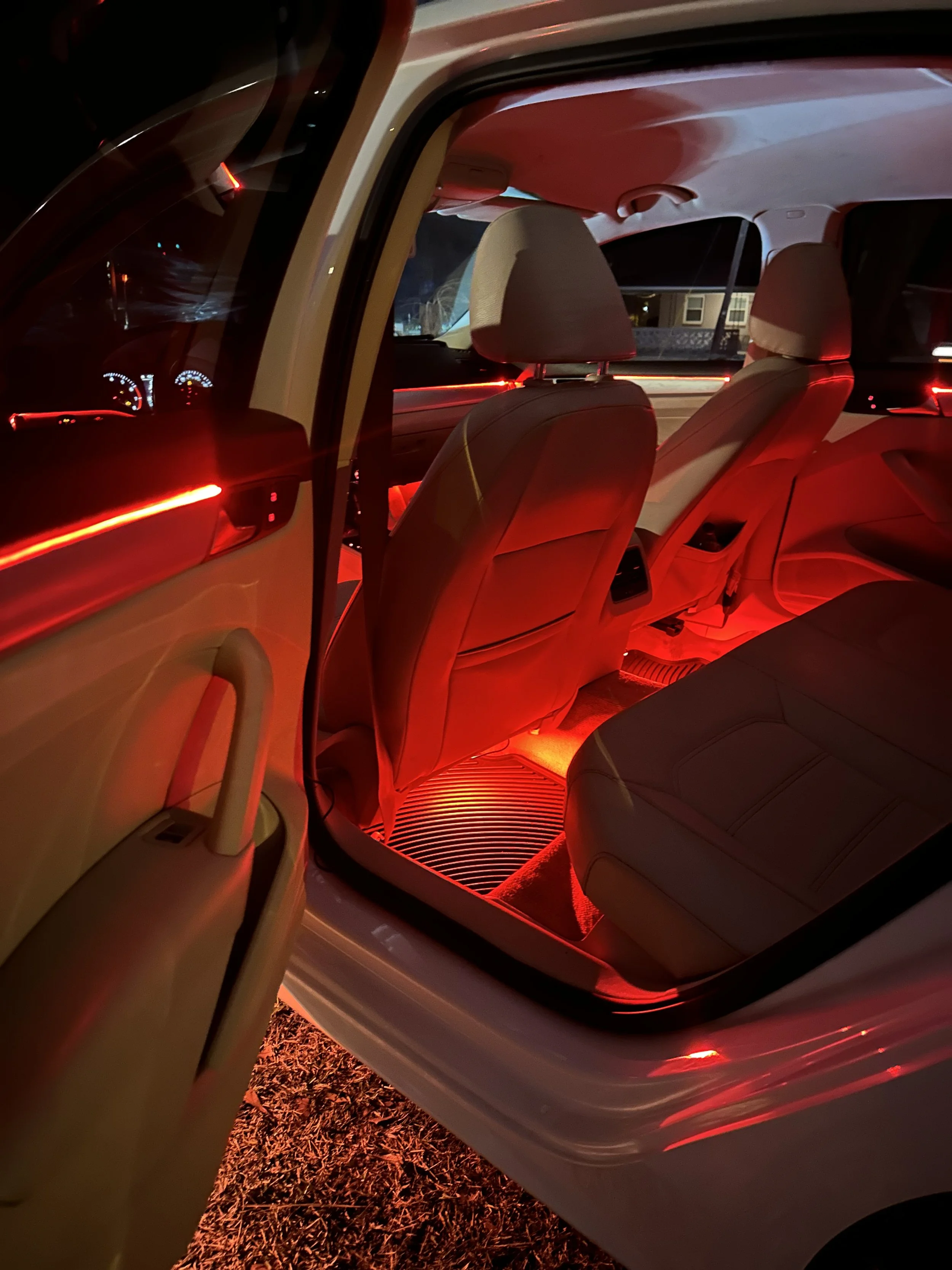 Car interior with red ambient lighting, open rear door, and illuminated seats and floor.