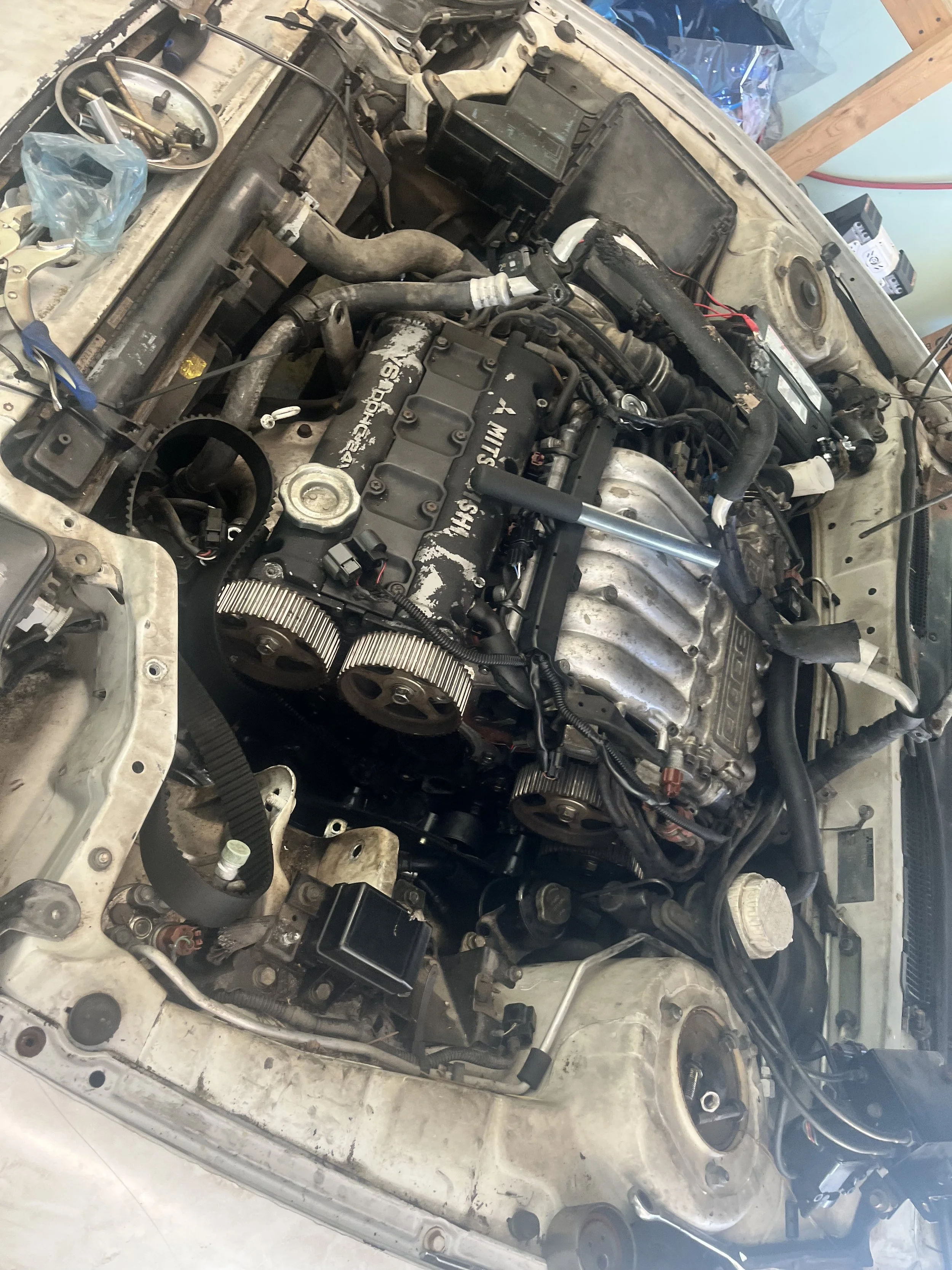 Open car hood showing a disassembled engine, tools, and parts scattered around.