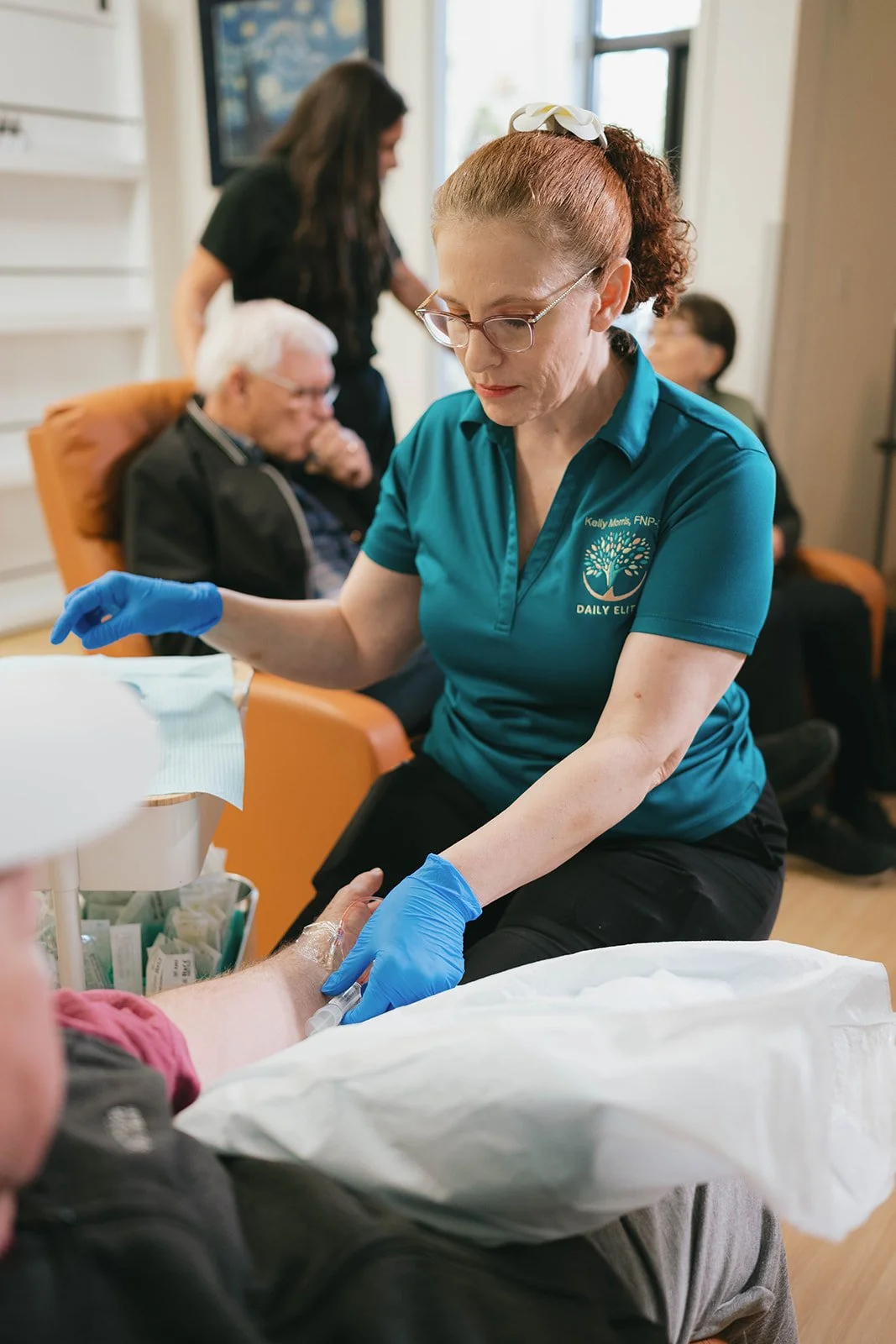 Nurse preparing to give an injection to a patient in a medical setting, with other healthcare workers and patients in the background.
