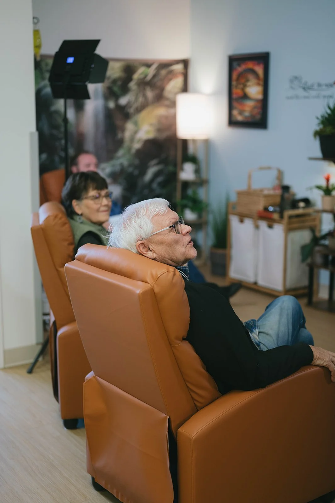 Three elderly people sitting in orange armchairs, watching something attentively in a cozy living room.