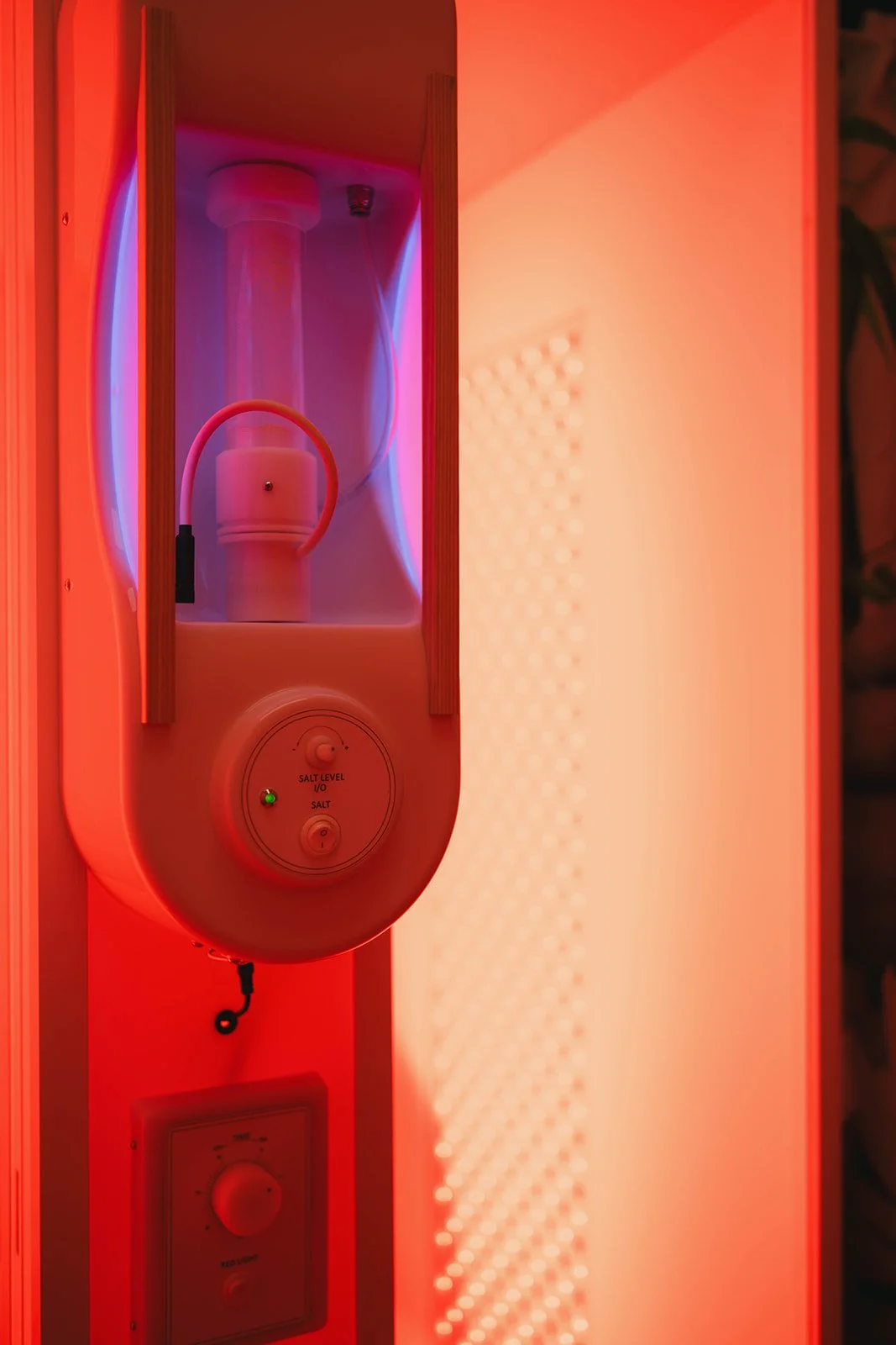 A modern salt therapy machine with a white cylindrical container and a pink tube inside a wooden frame, illuminated by red and purple lighting.