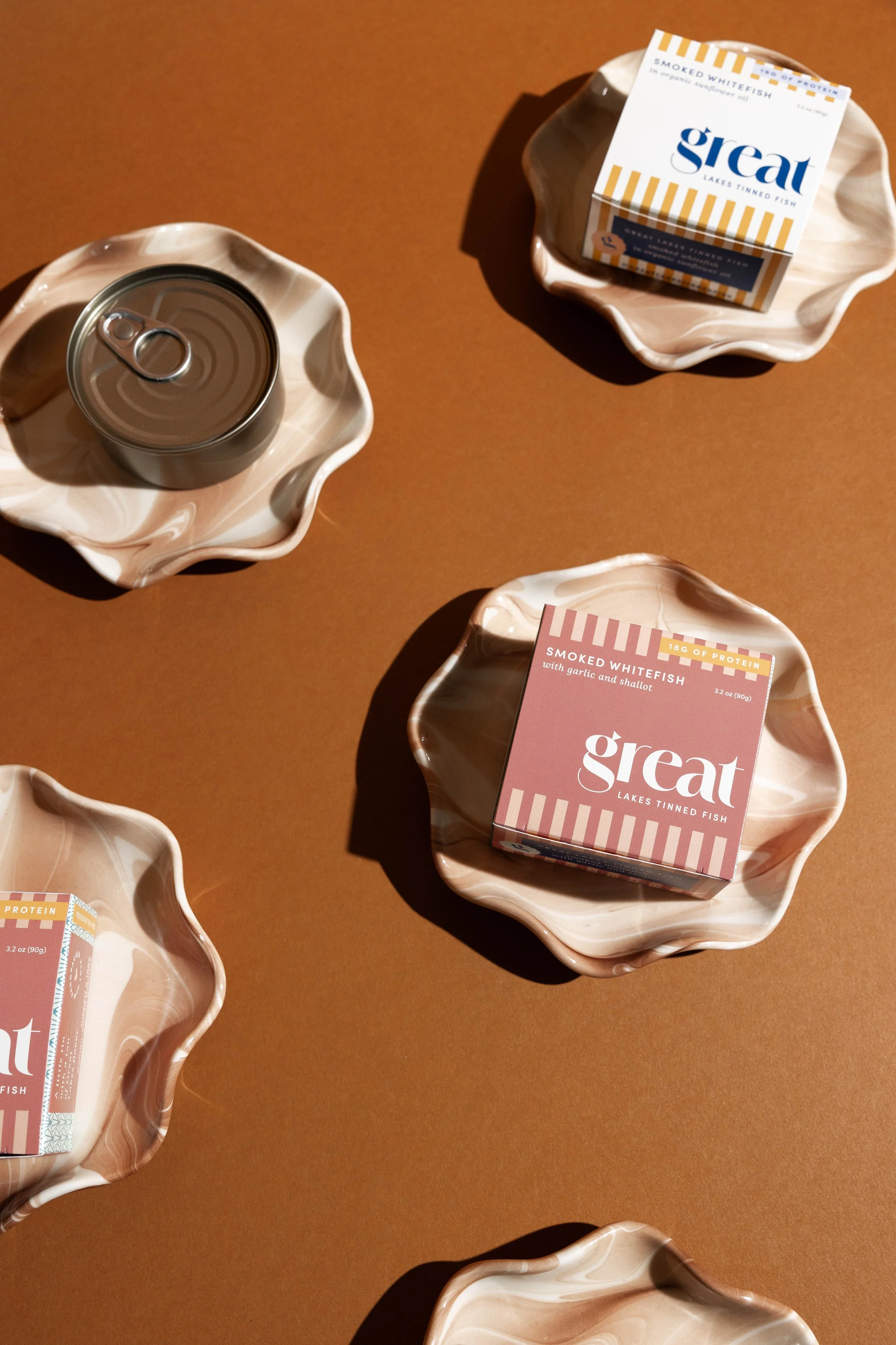 Tinned fish with packages and cans placed in decorative ceramic dishes on a brown background.