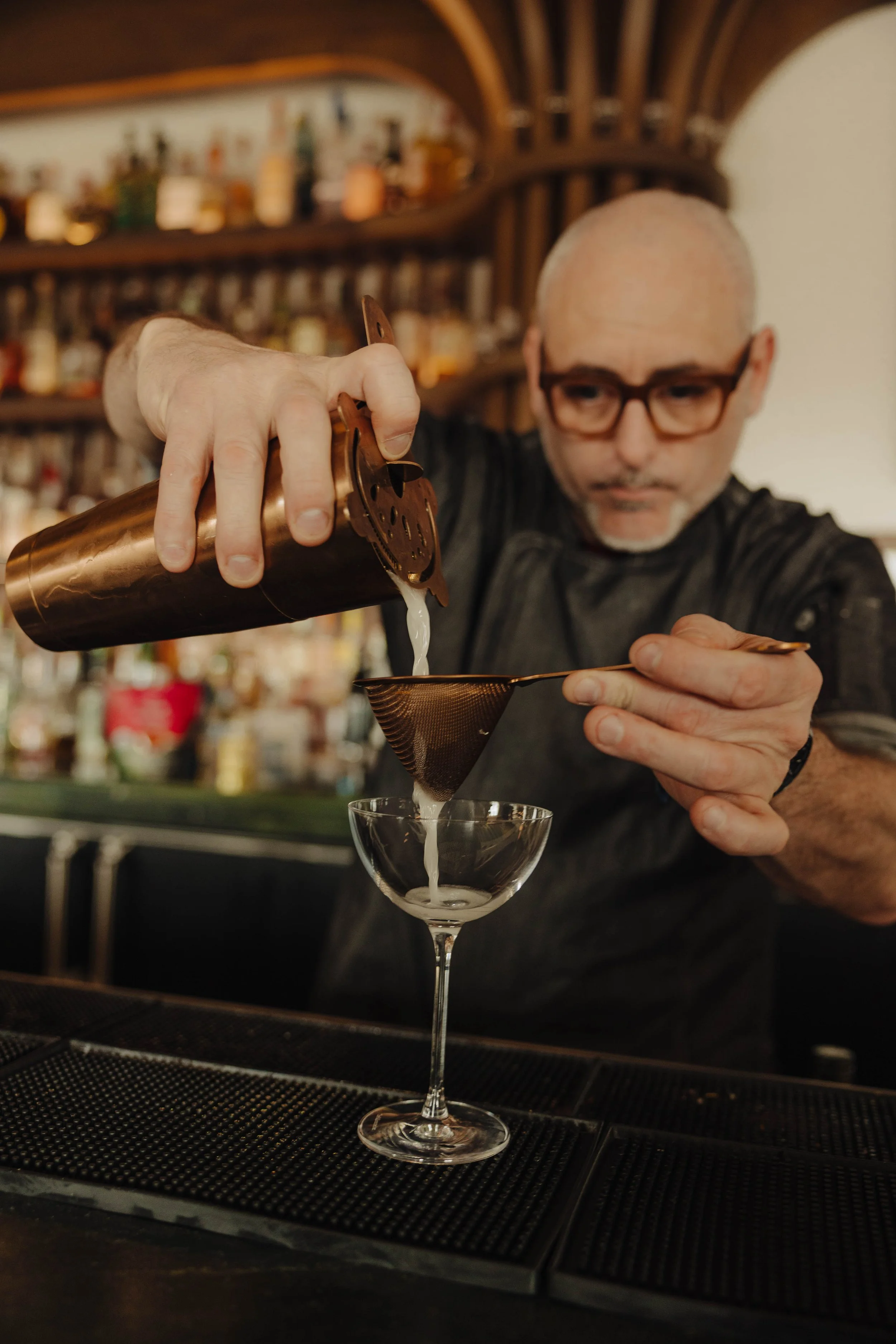Bartender pouring cocktail through strainer into glass