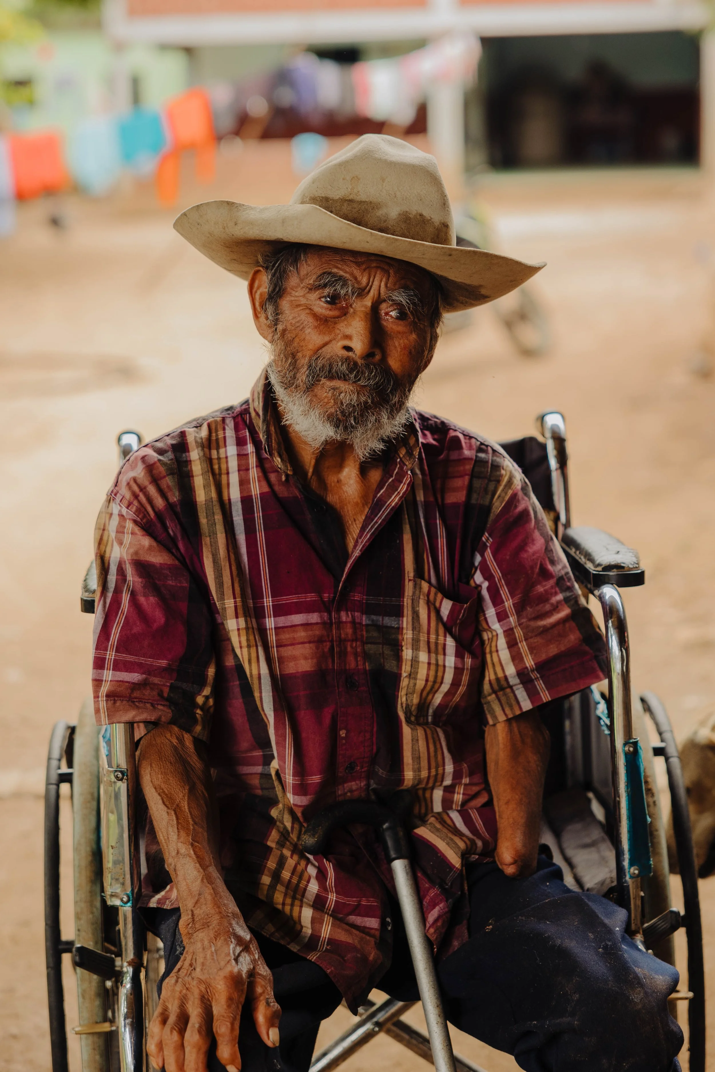 Senior man in a wheelchair wearing a cowboy hat and plaid shirt.