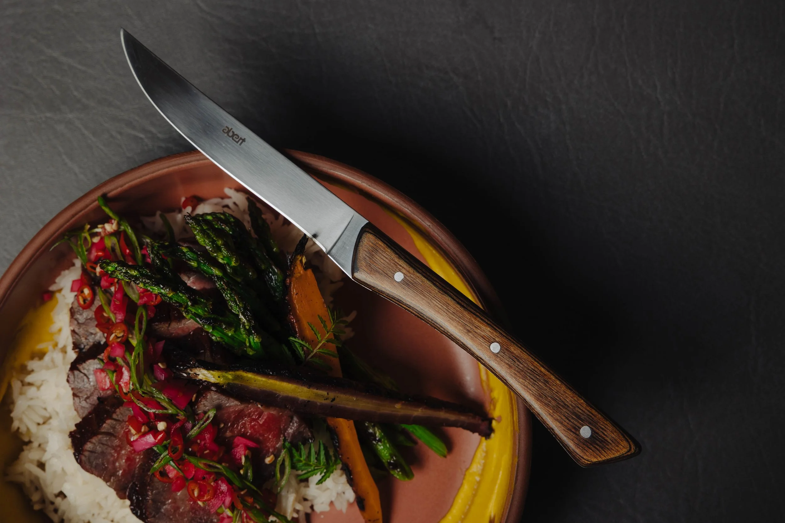 Food dish with rice, asparagus, beef, sliced peppers, and a knife on a plate.