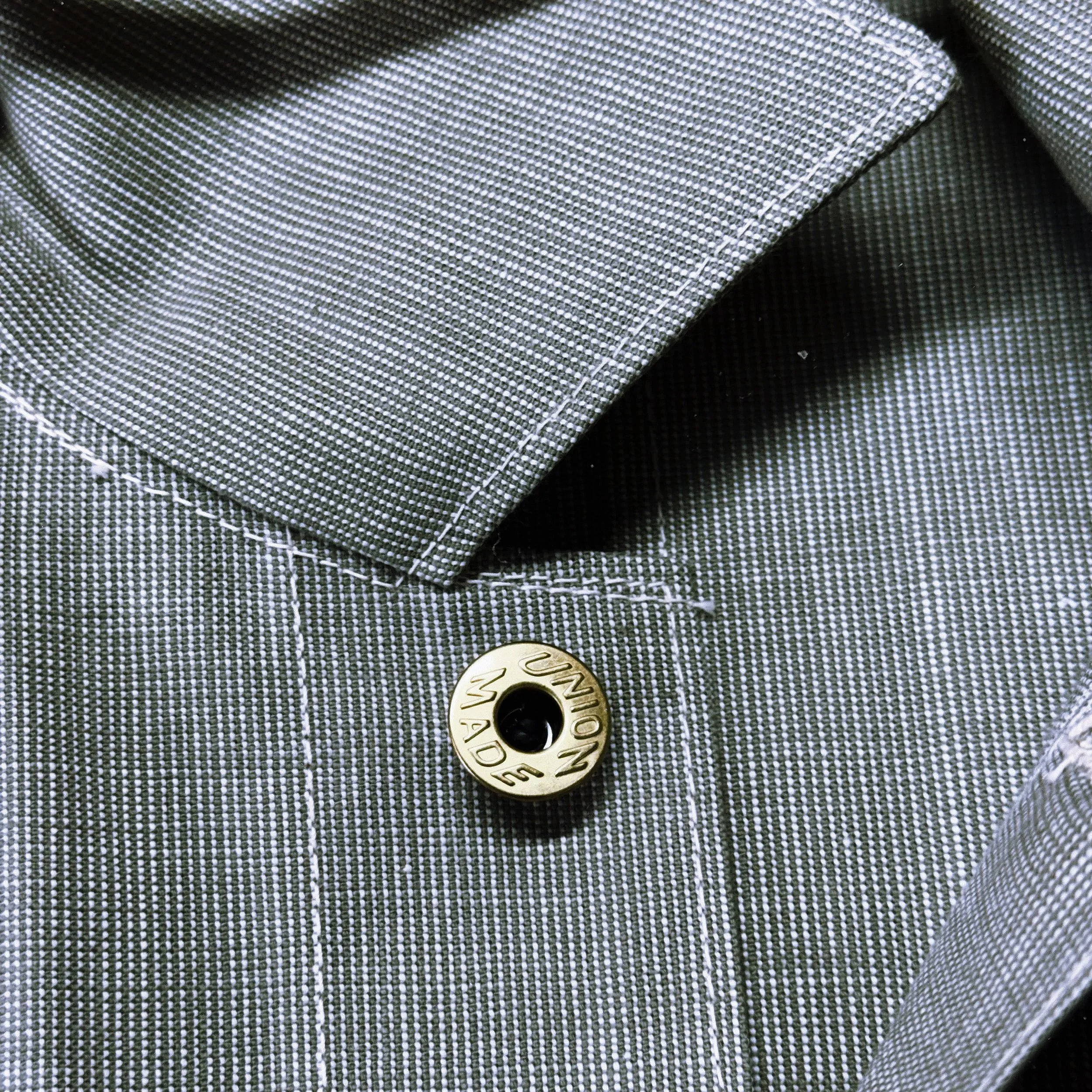 Close-up of the neck of an early 1900’s inspired chore coat with a branded gold button that reads 'UNION MADE'.