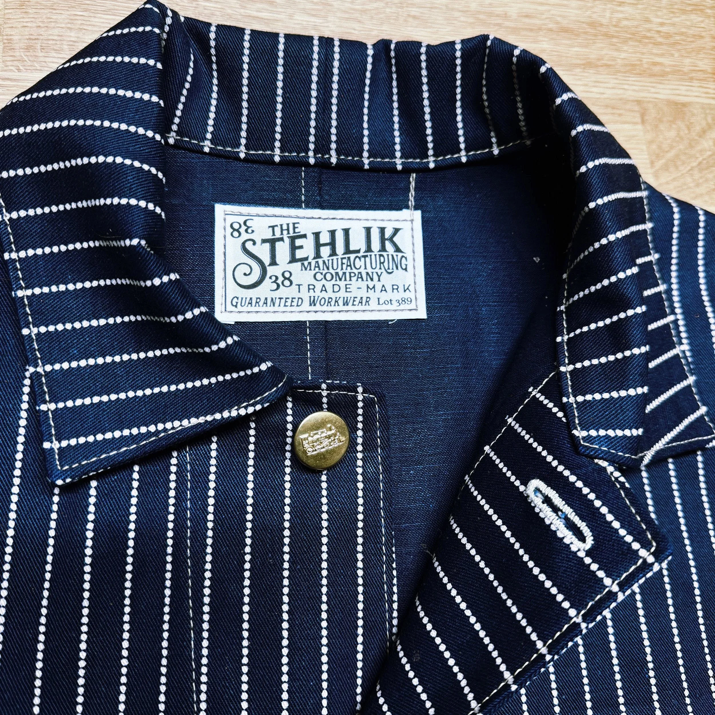 Close-up of an early 1900’s Wabash chore coat, featuring a label that reads “The Stehlik Manufacturing Company, Guaranteed Workwear, Lot 389” and a metal button with an embossed train motif.