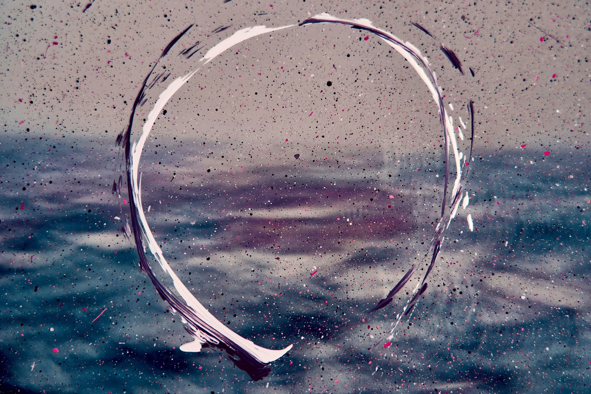 A heart shape drawn in pink paint on a speckled, sandy beach with the ocean in the background.