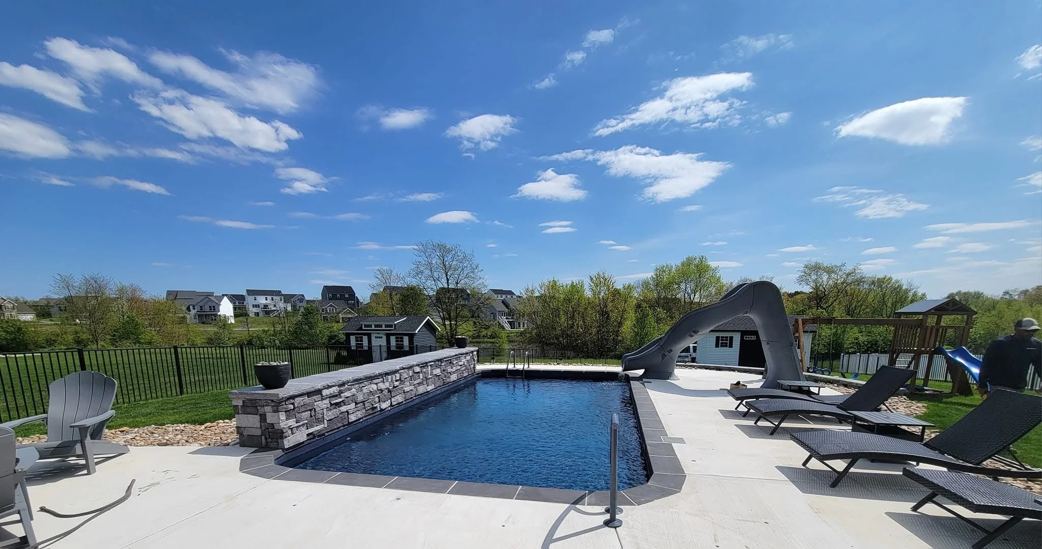 Backyard with swimming pool, slide, lounge chairs, and a playset.
