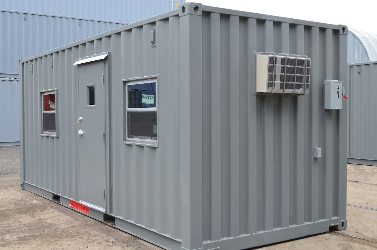 Gray shipping container modified into a mobile office with windows, door, and exterior air conditioning unit.