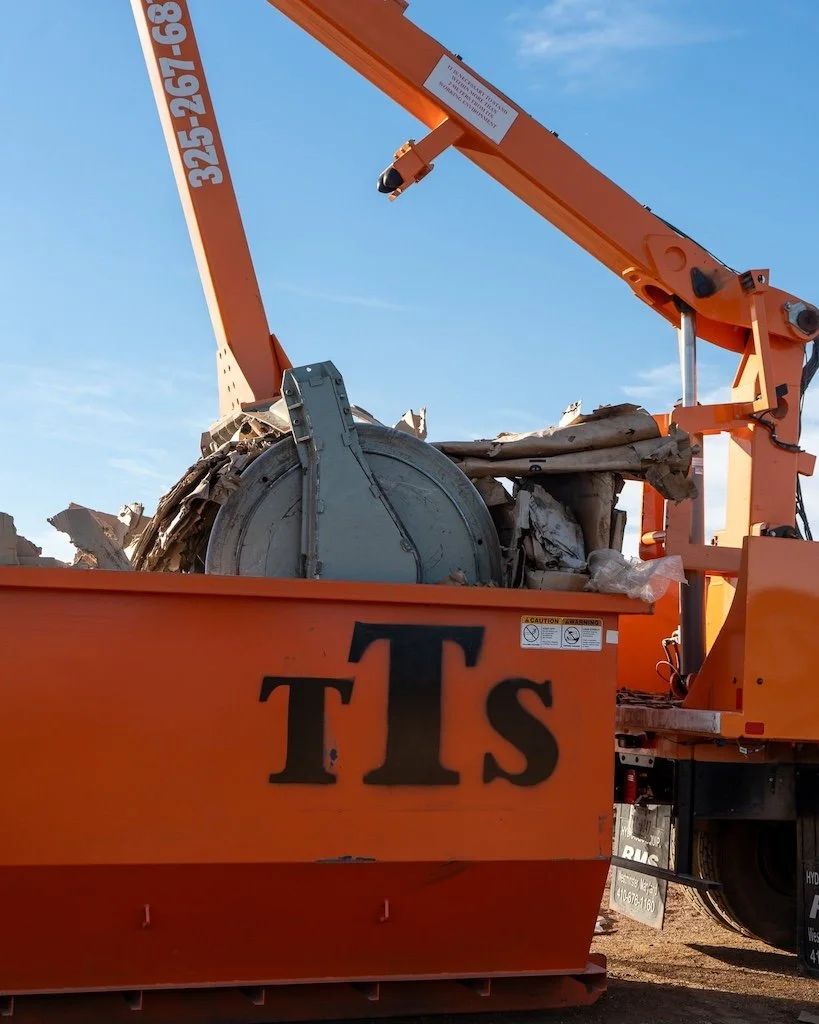Orange construction equipment with a labeled dumpster containing debris under a blue sky.