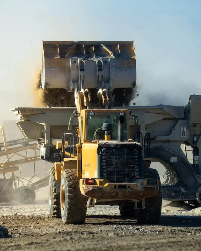 Front loader dumping soil into a large machine on a construction site.