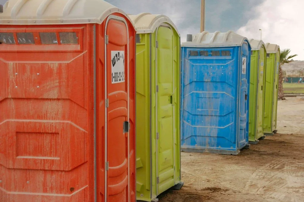 Row of colorful portable toilets on dirt ground with overcast sky.