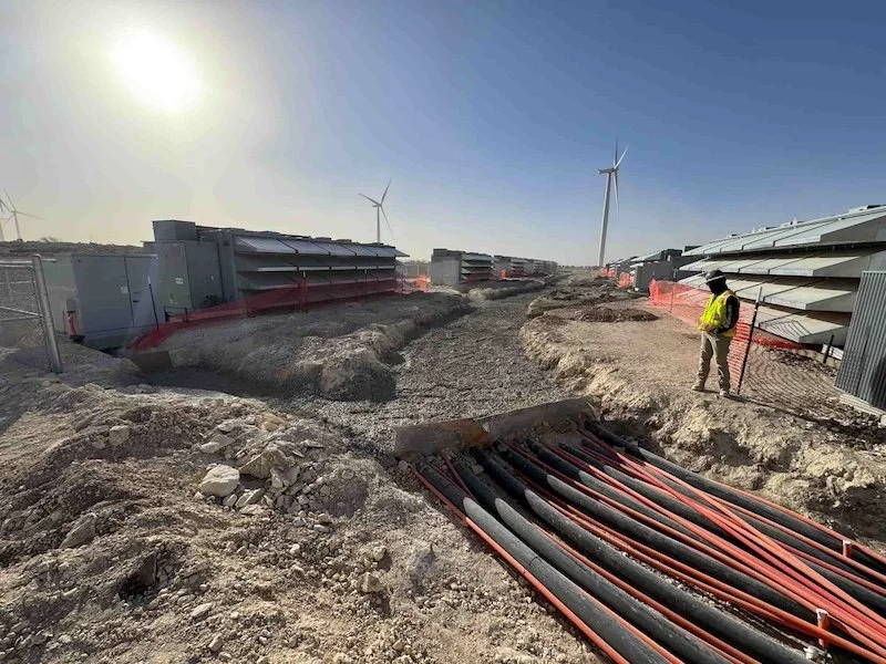 Construction site with wind turbines and a worker in a safety vest, showing electrical cables and industrial infrastructure.