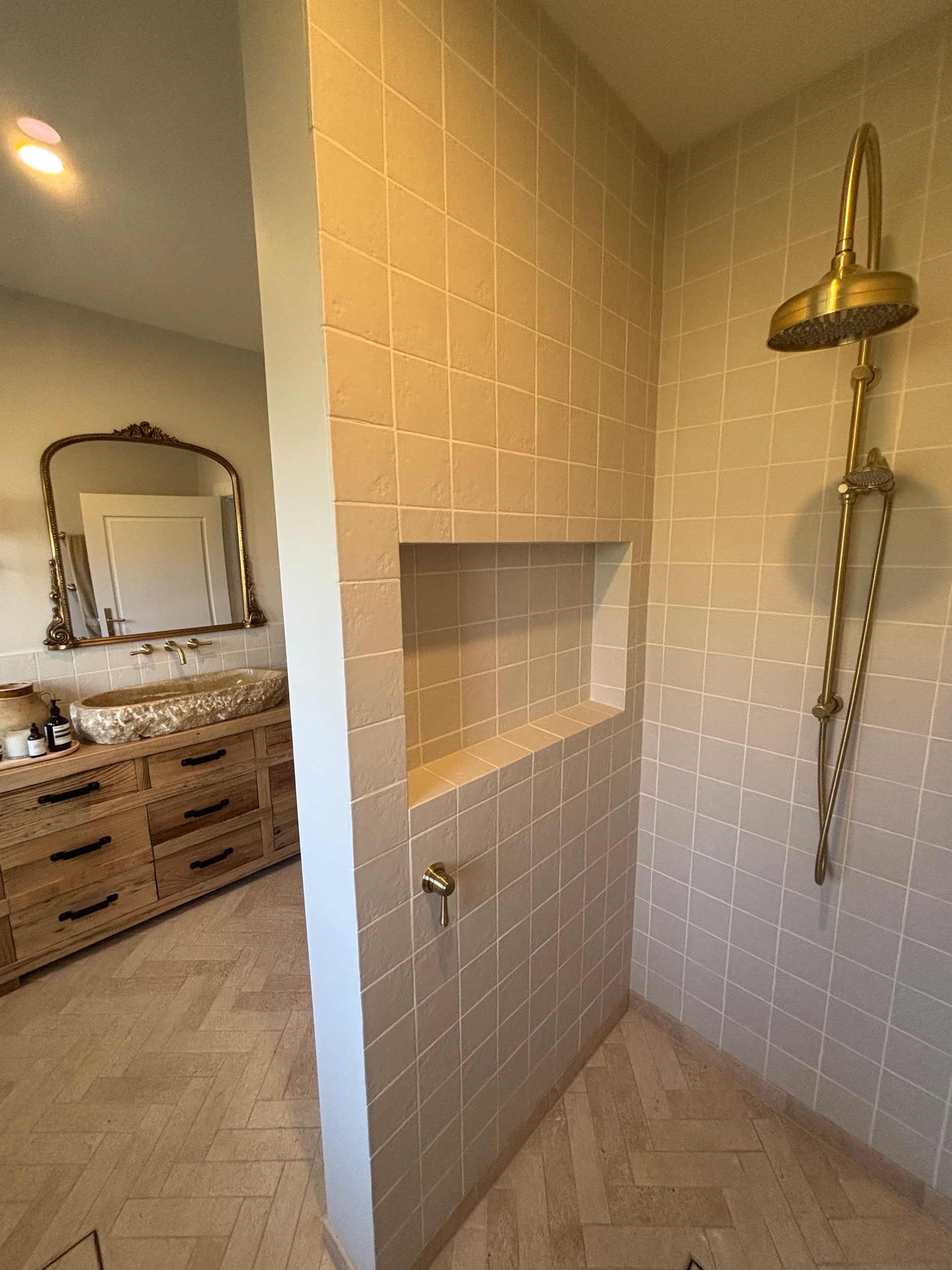 Bathroom renovation in the Southern Highlands, NSW with standalone shower featuring a brass showerhead and rail, beige tiled walls, and a wooden vanity with a marble countertop and mirror.