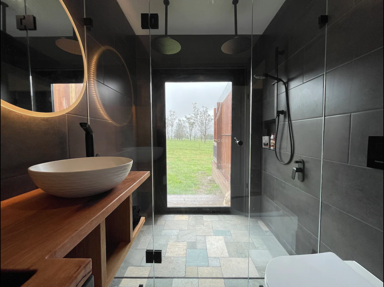 Bathroom Renovation depicting timber accents, earthy stone colours and soft diffused lighting with a window overlooking the Southern Highlands