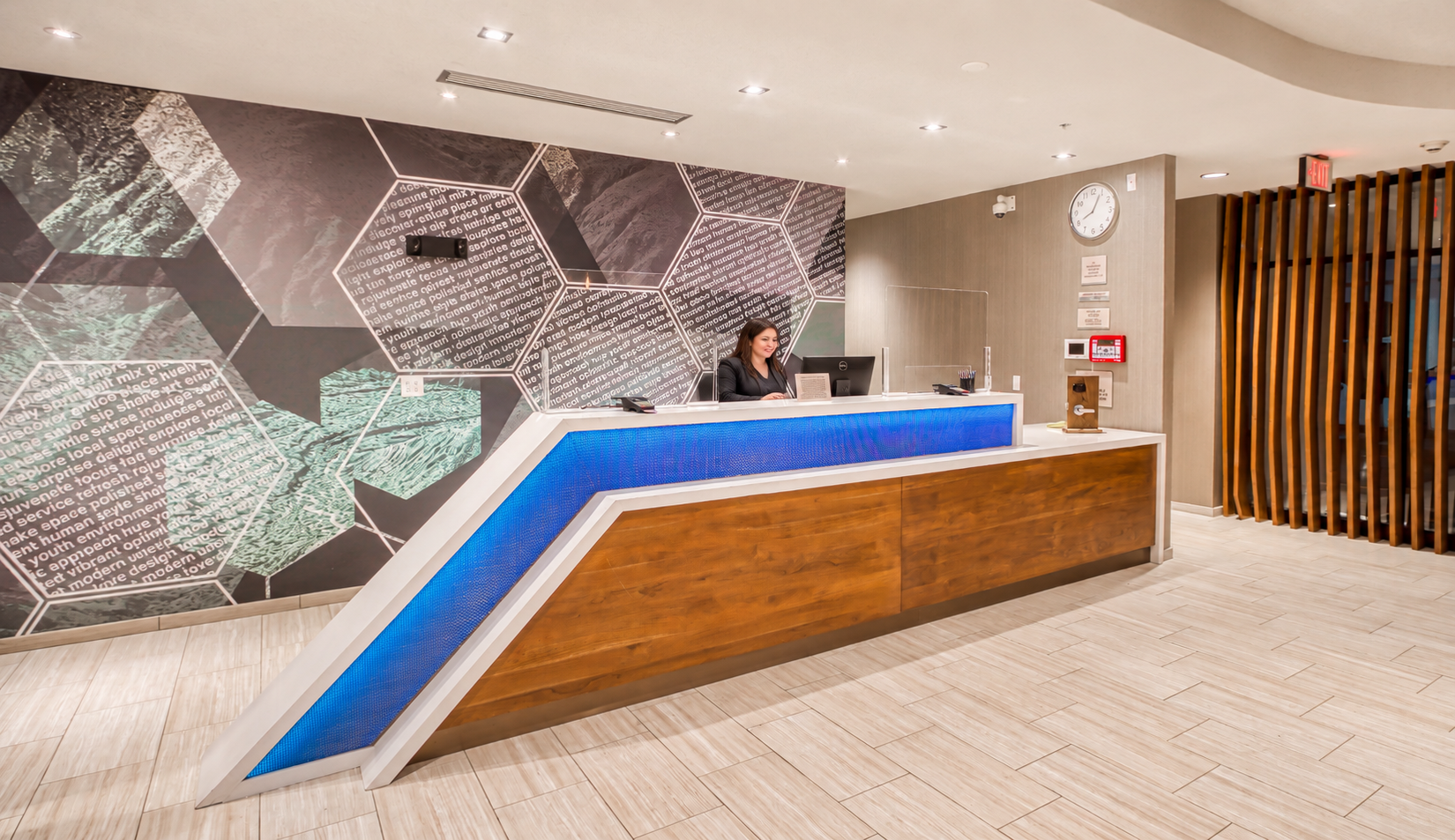 Modern hotel lobby reception desk with geometric wall art, warm lighting, and a blue illuminated counter.