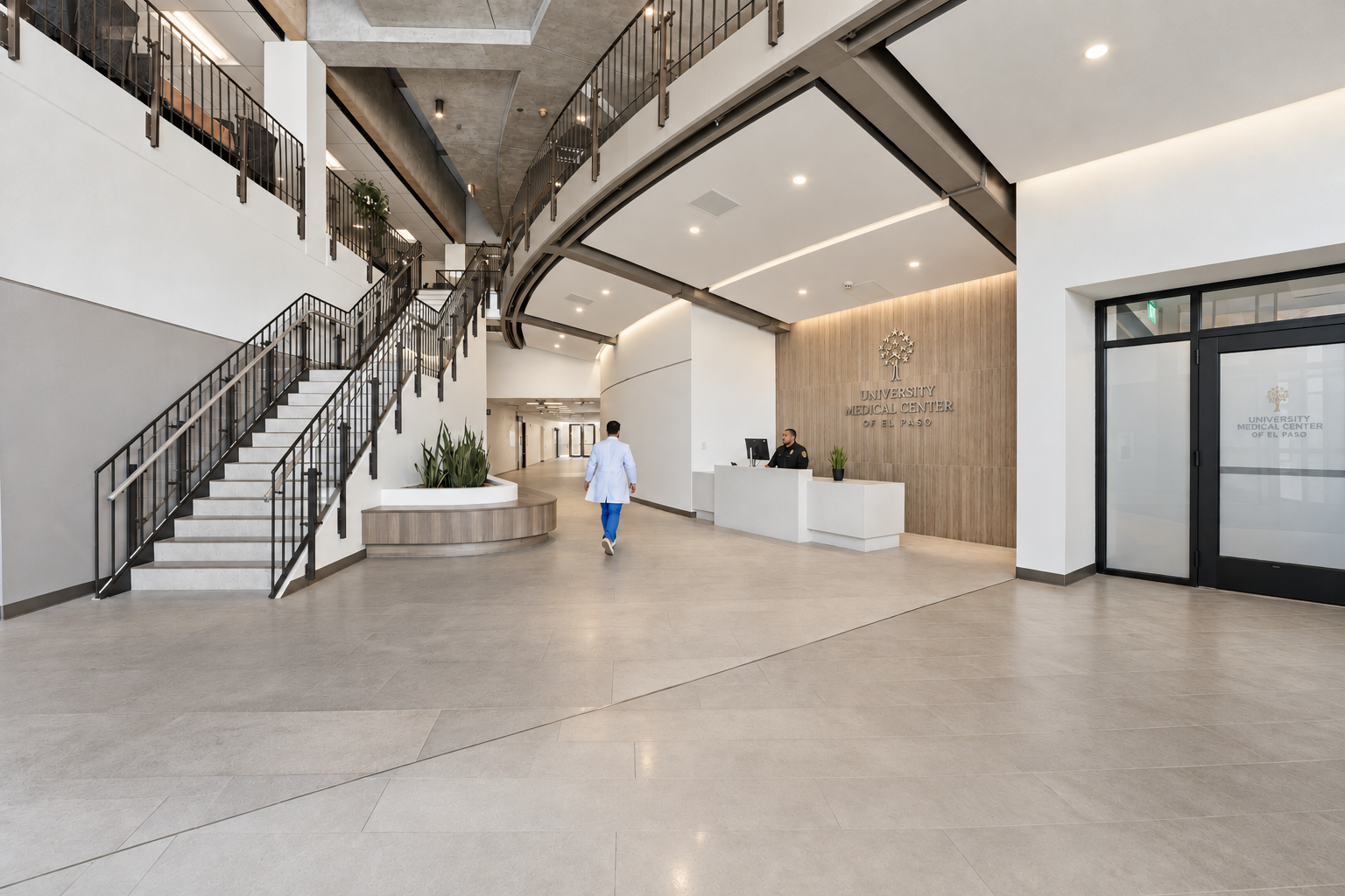 Modern university campus lobby with seating area, reception desk, glass entrance, and stairs, with people seated and walking.