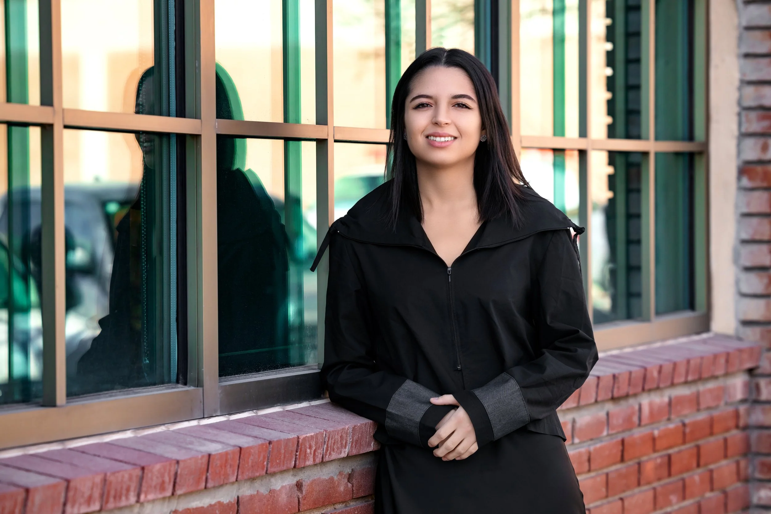 Young woman with shoulder-length dark hair, smiling, in front of a colorful fence background.