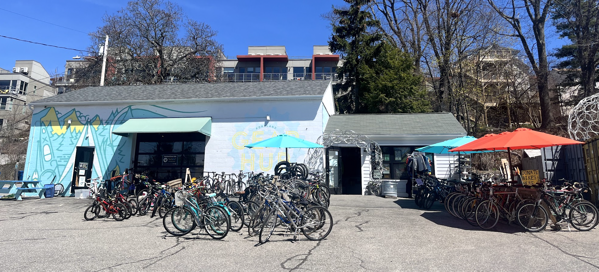 Photo of a building on a sunny day with blue sky with many bicycles of all kinds in front of it.