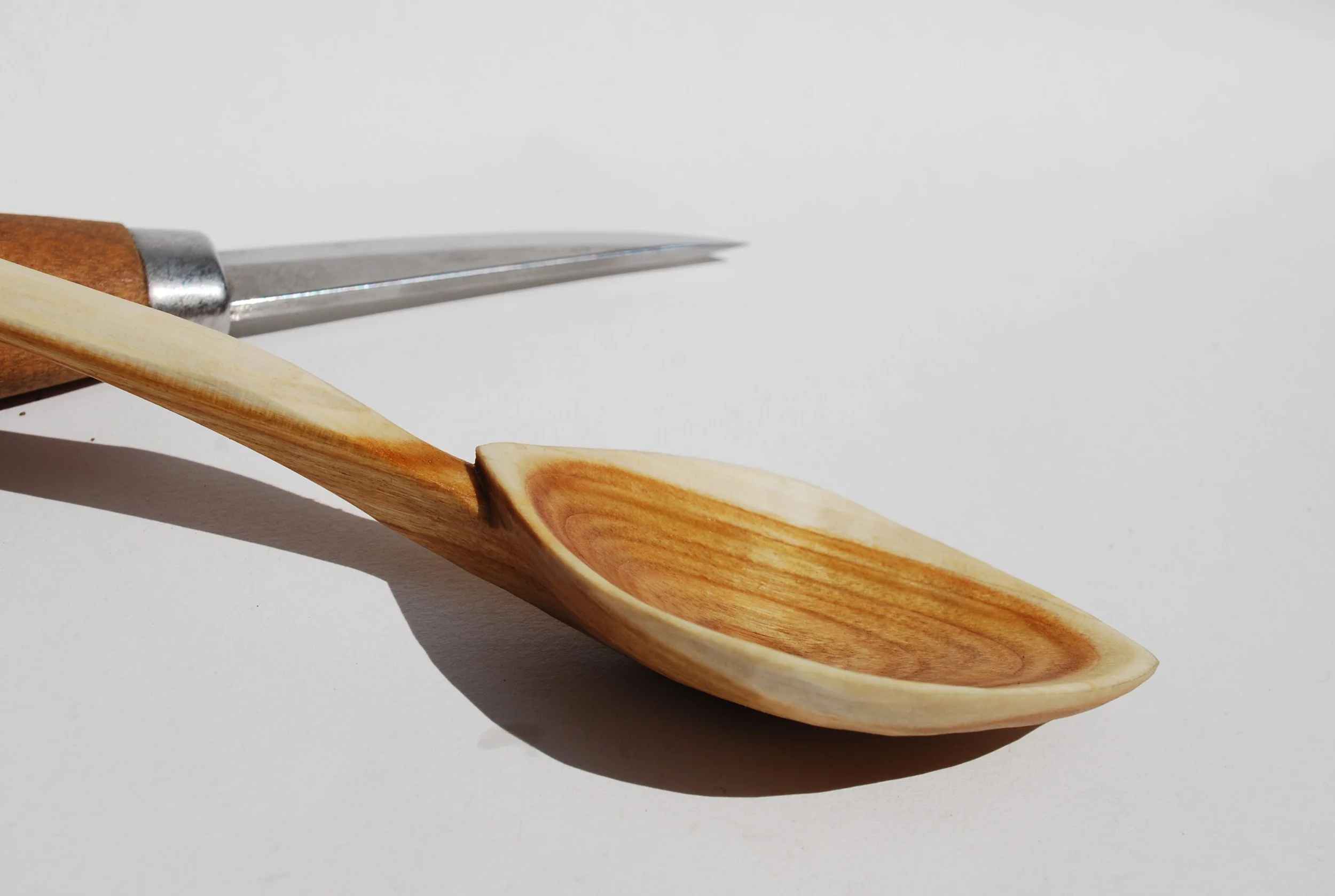 A wooden spoon and a carving tool on a white background.