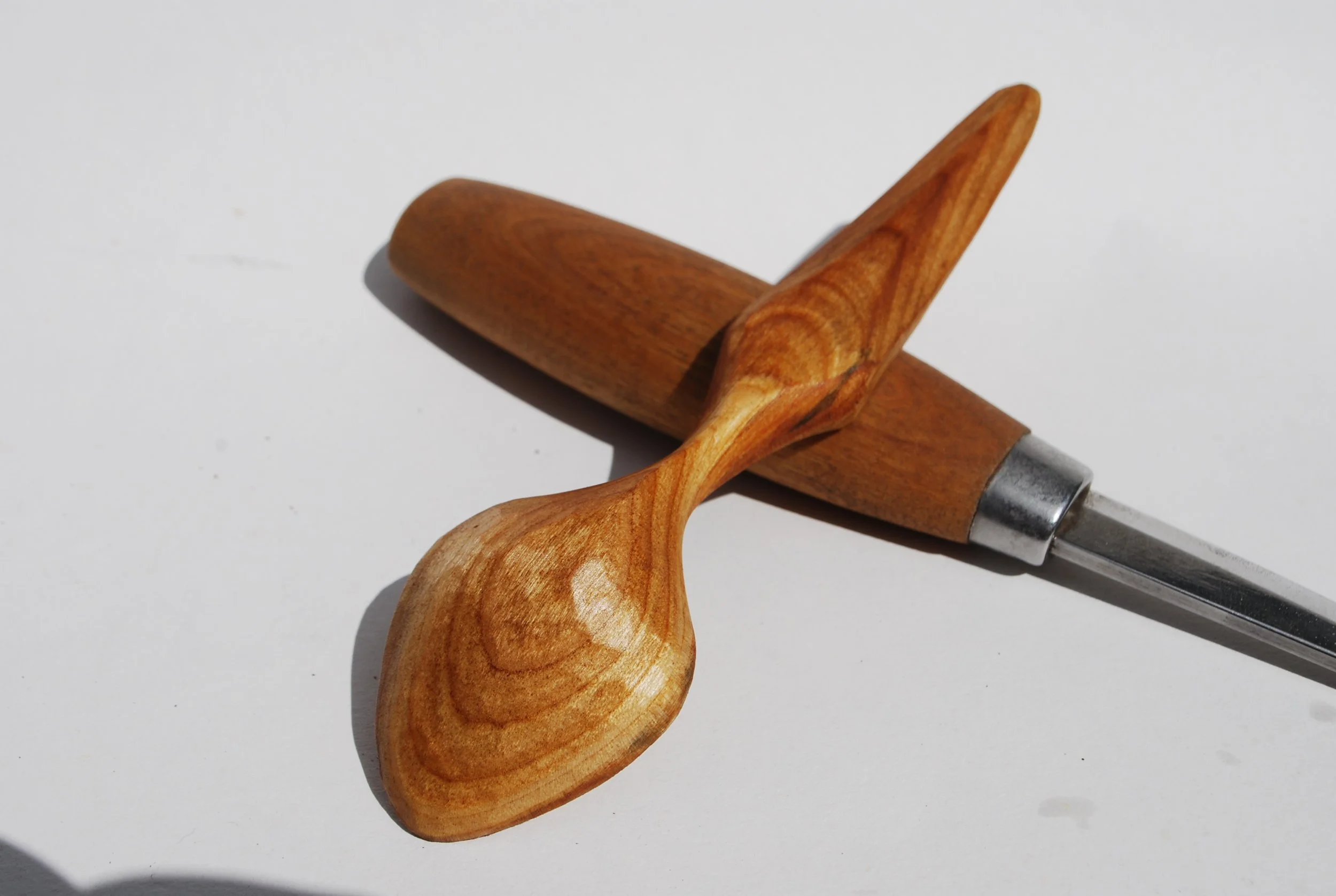 A wooden spoon and a wooden-handled knife on a white surface.