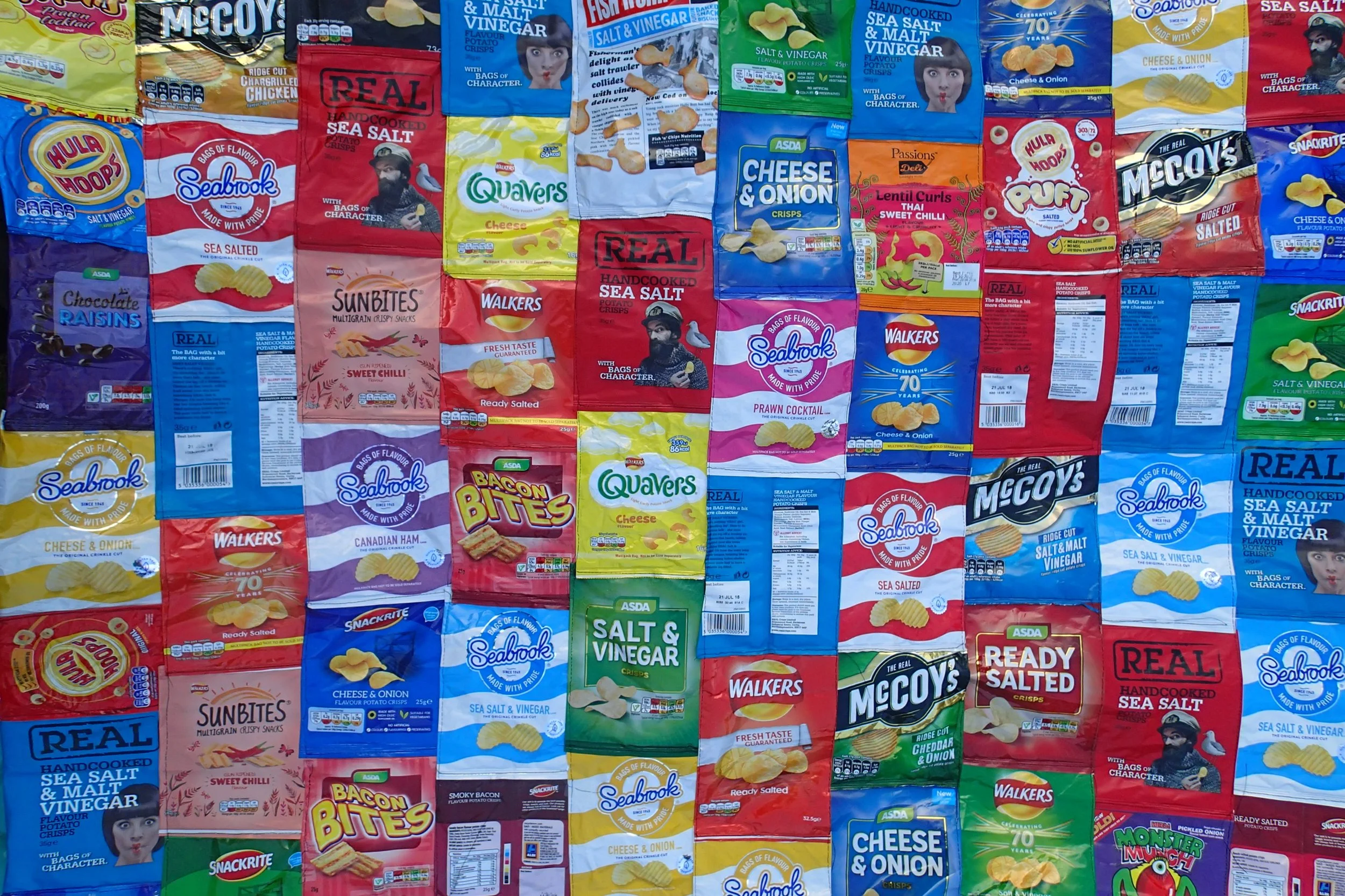 A collage of various snack food packages, mainly chips and crisps, including brands like Seabrook, McCoy's, Walker's, and McDonald's, arranged in overlapping rows and columns.