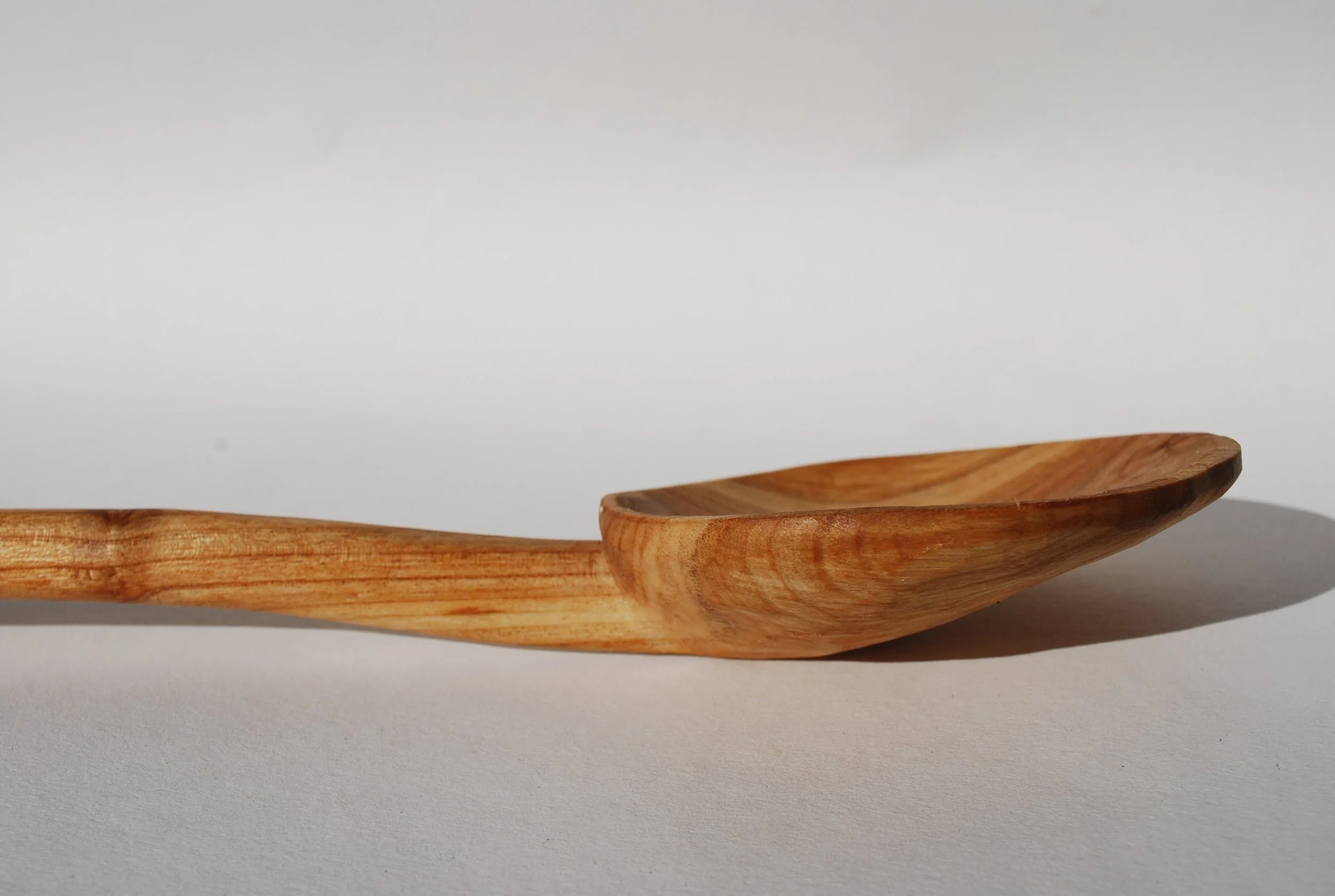 A close-up of a wooden spoon lying on a white surface with shadow cast to the right.