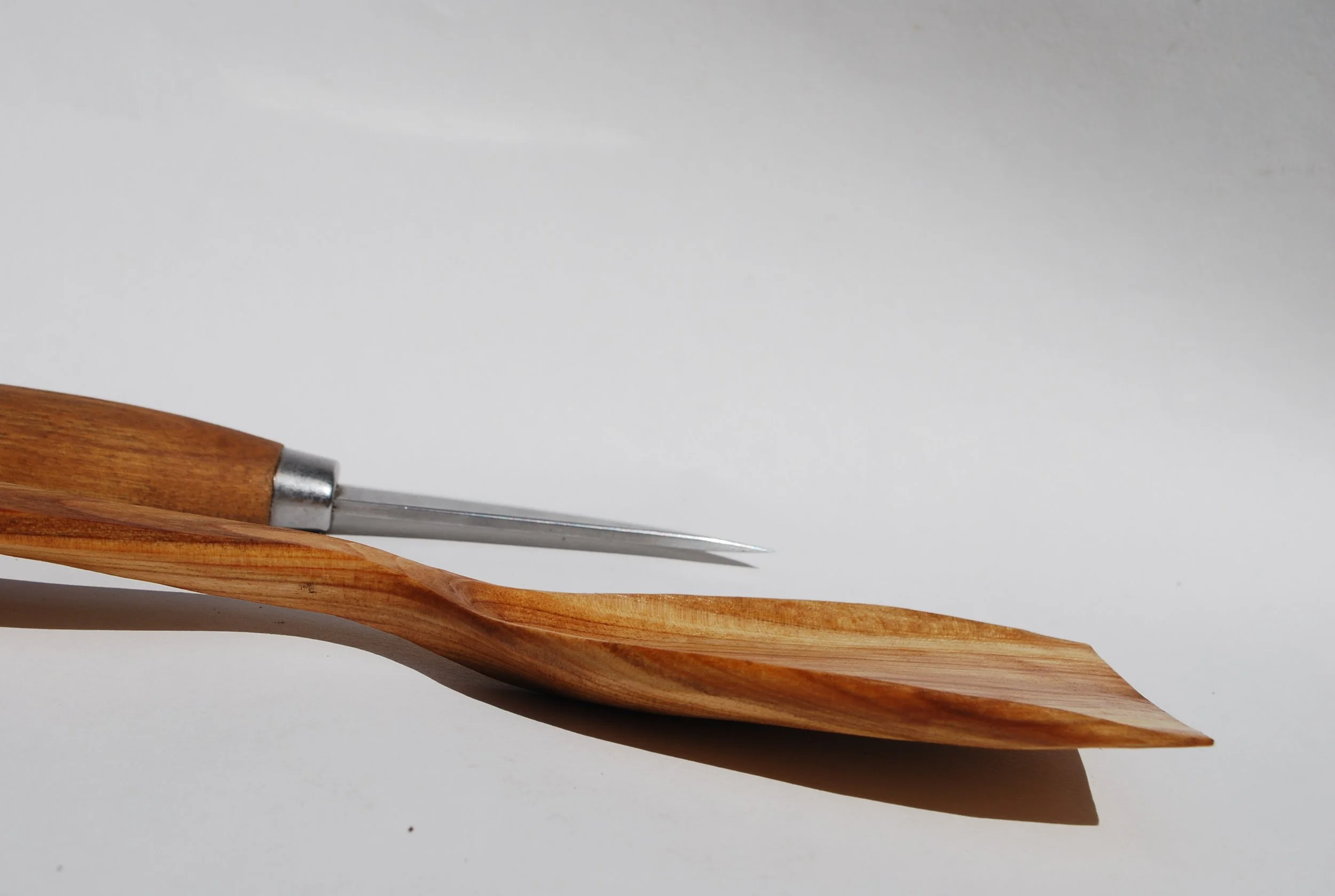 A wooden spatula with a metal and wooden carving tool resting on it, set on a white surface.