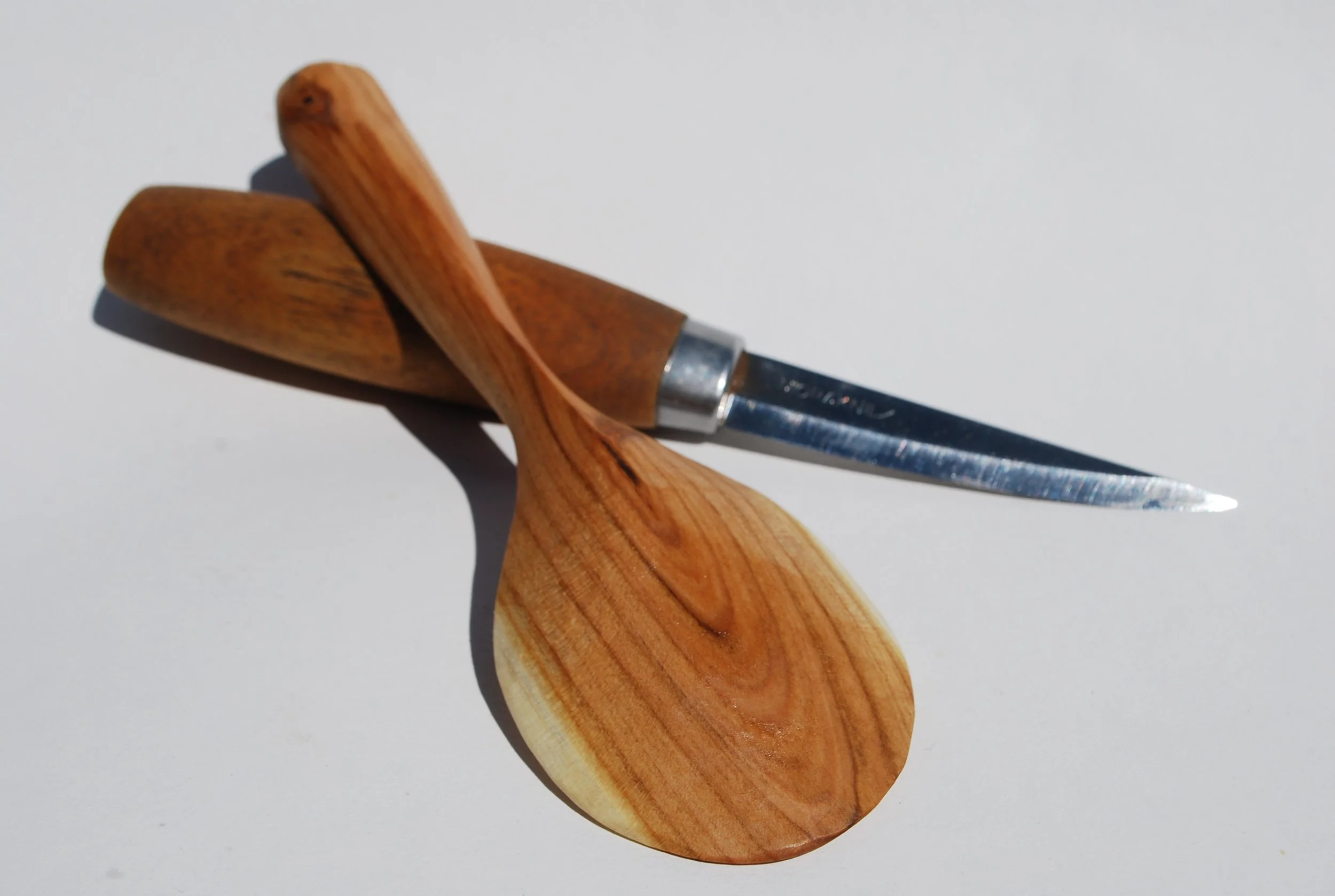 A wooden-handled starting knife resting on a matching wooden spoon, with the knife blade pointing to the right.