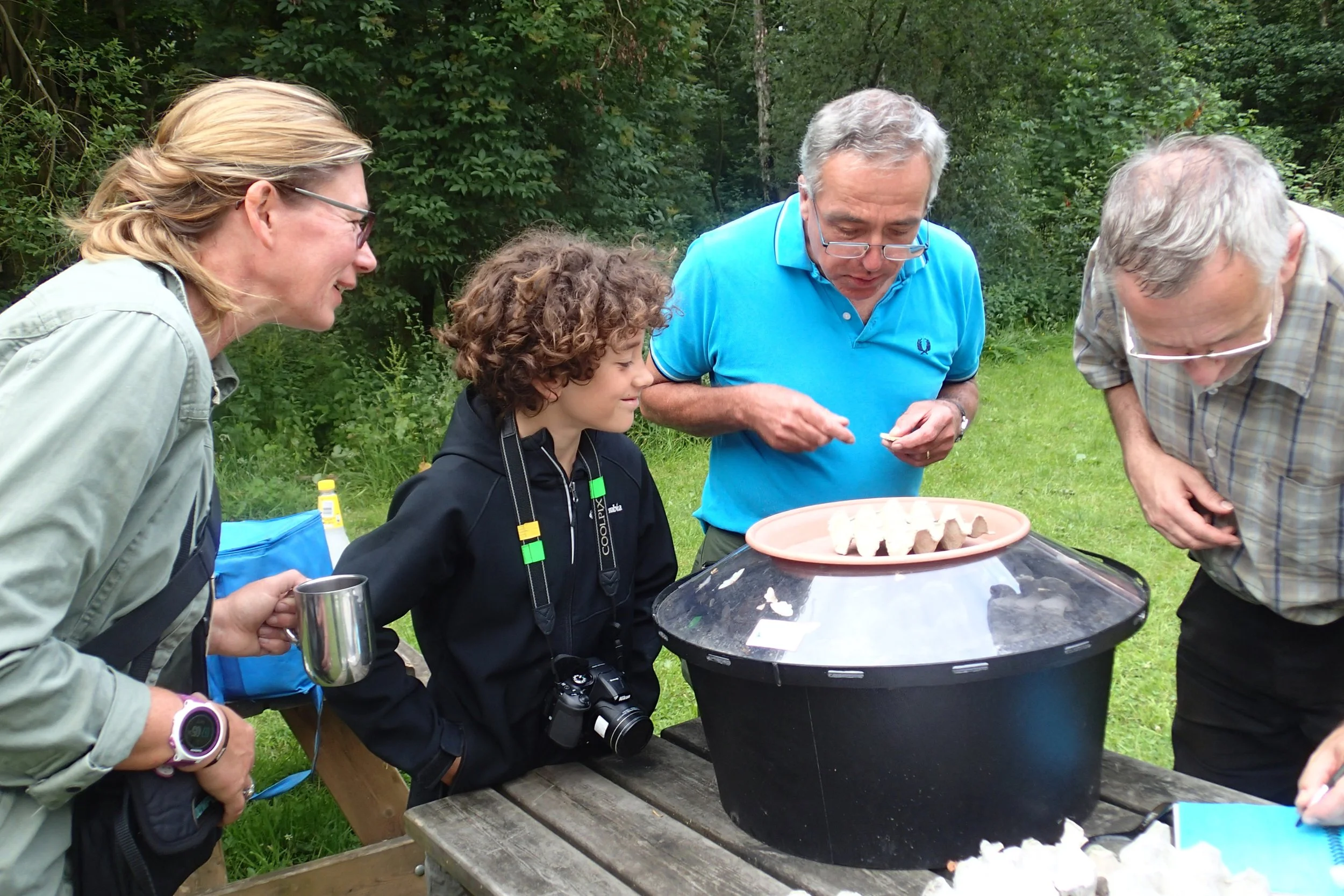 Group of five people examining eggs in an outdoor setting with trees and grass in the background.
