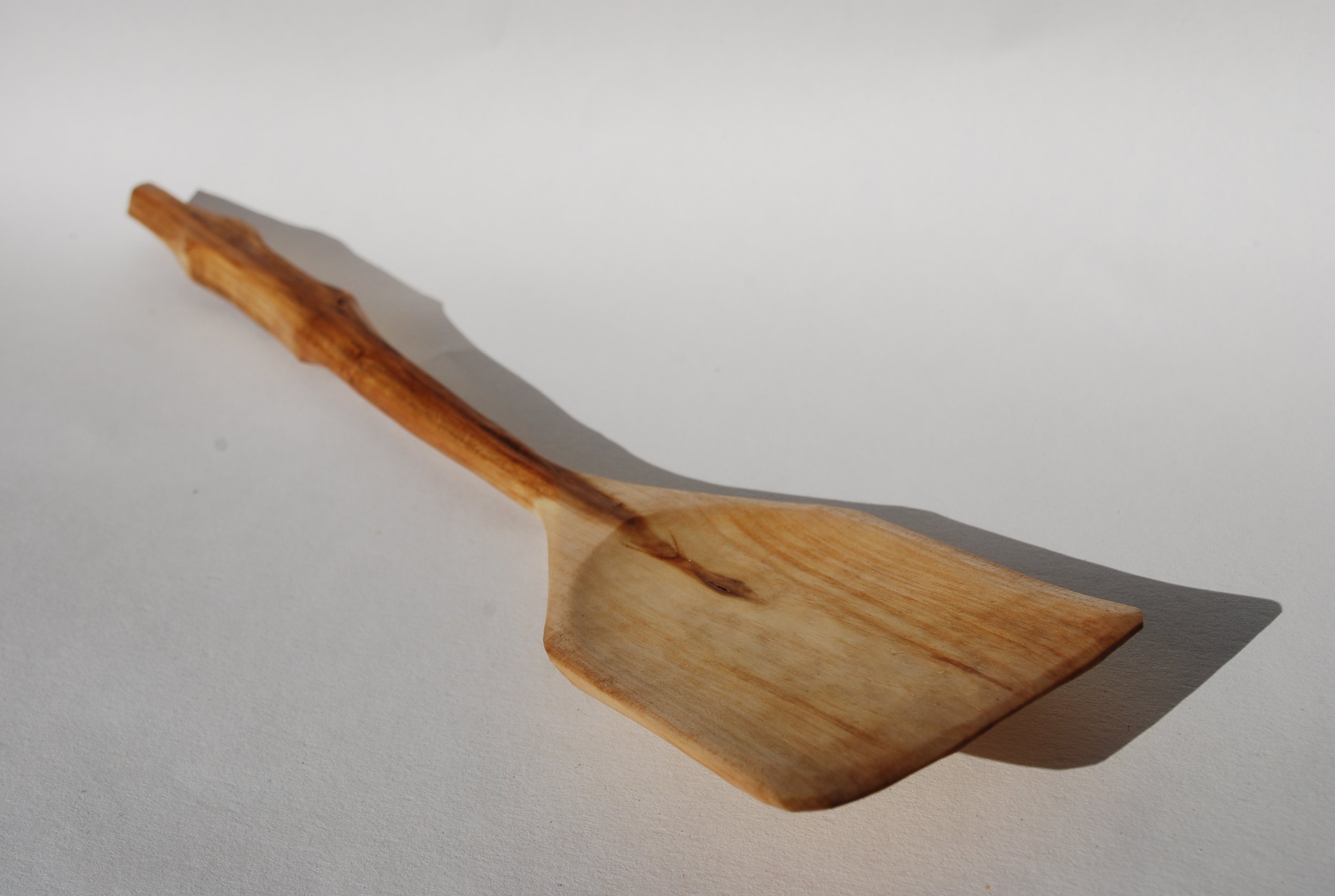 A wooden spatula resting on a white surface, casting a shadow to the right.