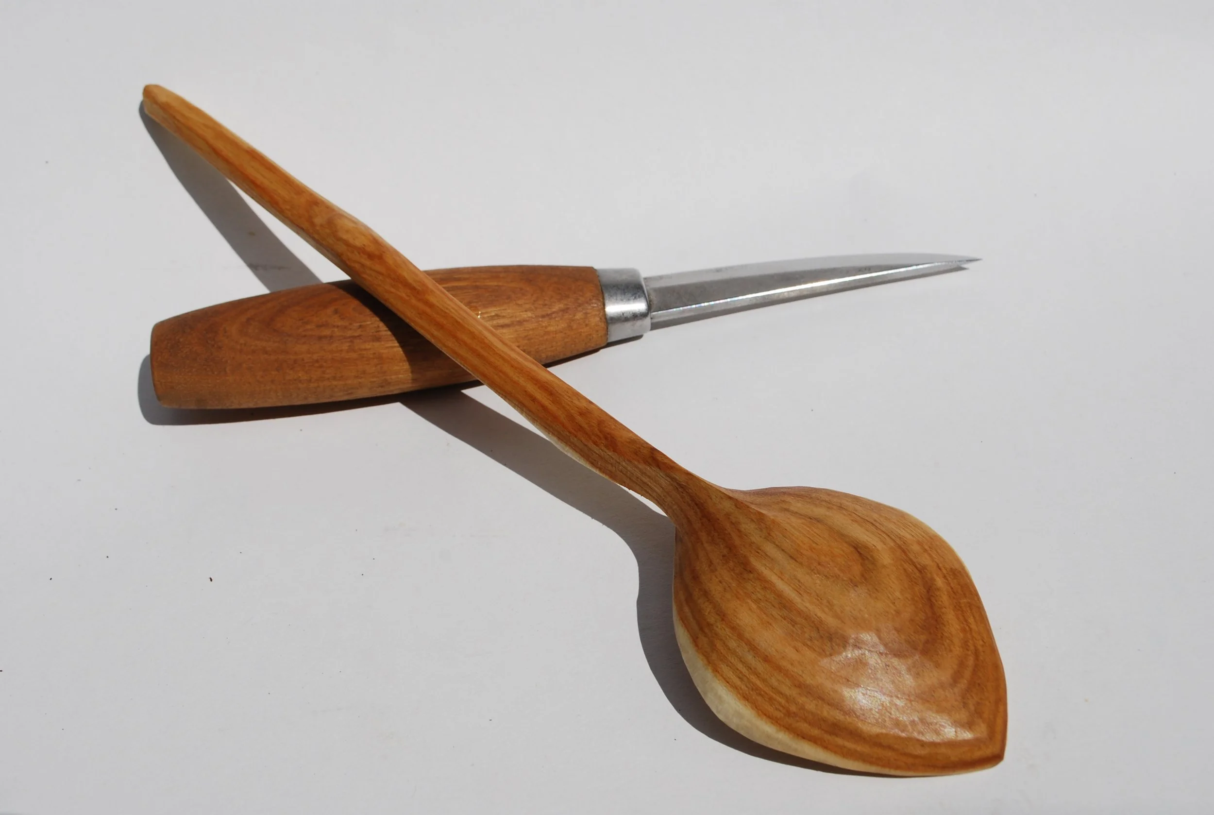 A wooden spoon, a wooden spatula, and a small knife with a wooden handle on a white surface.