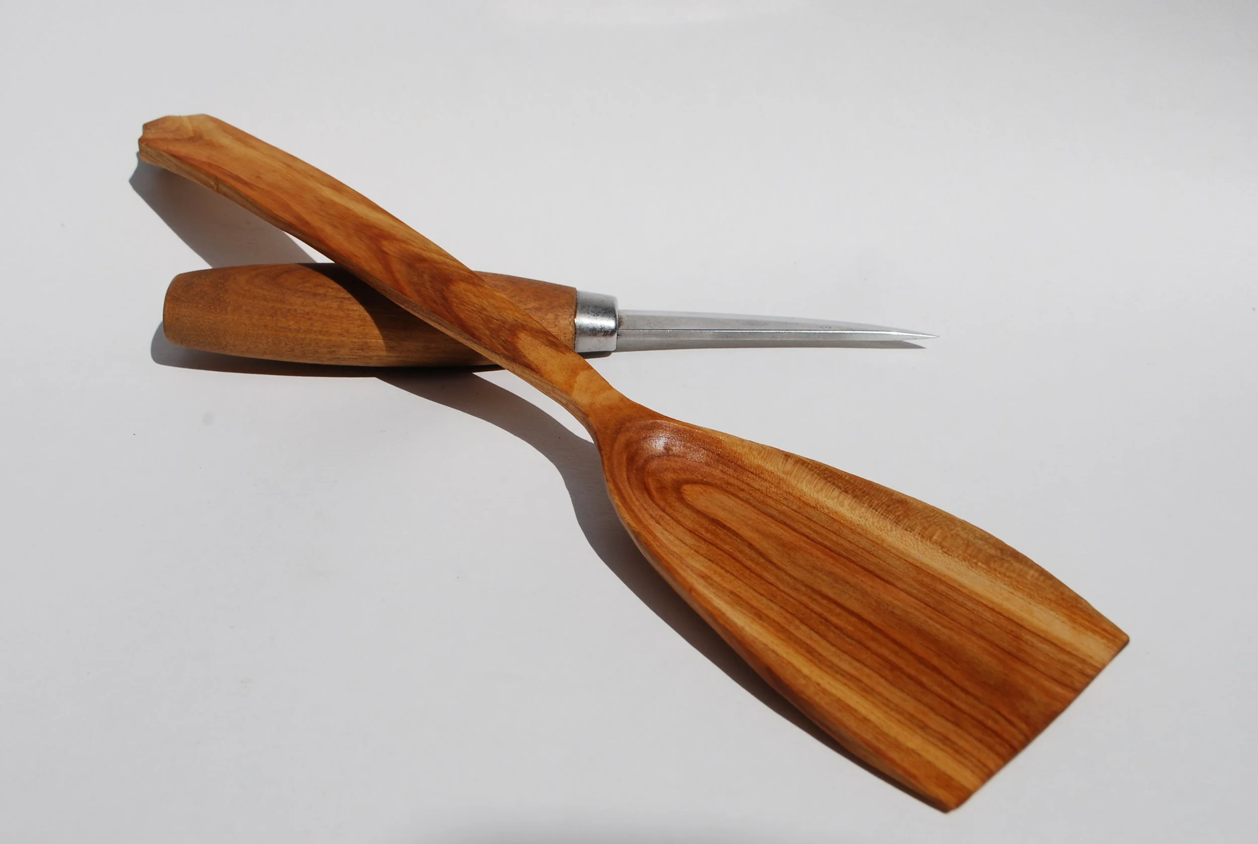 A wooden-handled spoon and a metal awl on a white surface.
