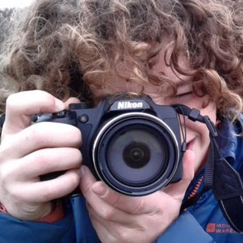 Person with curly hair holding a Nikon camera and taking a photo.
