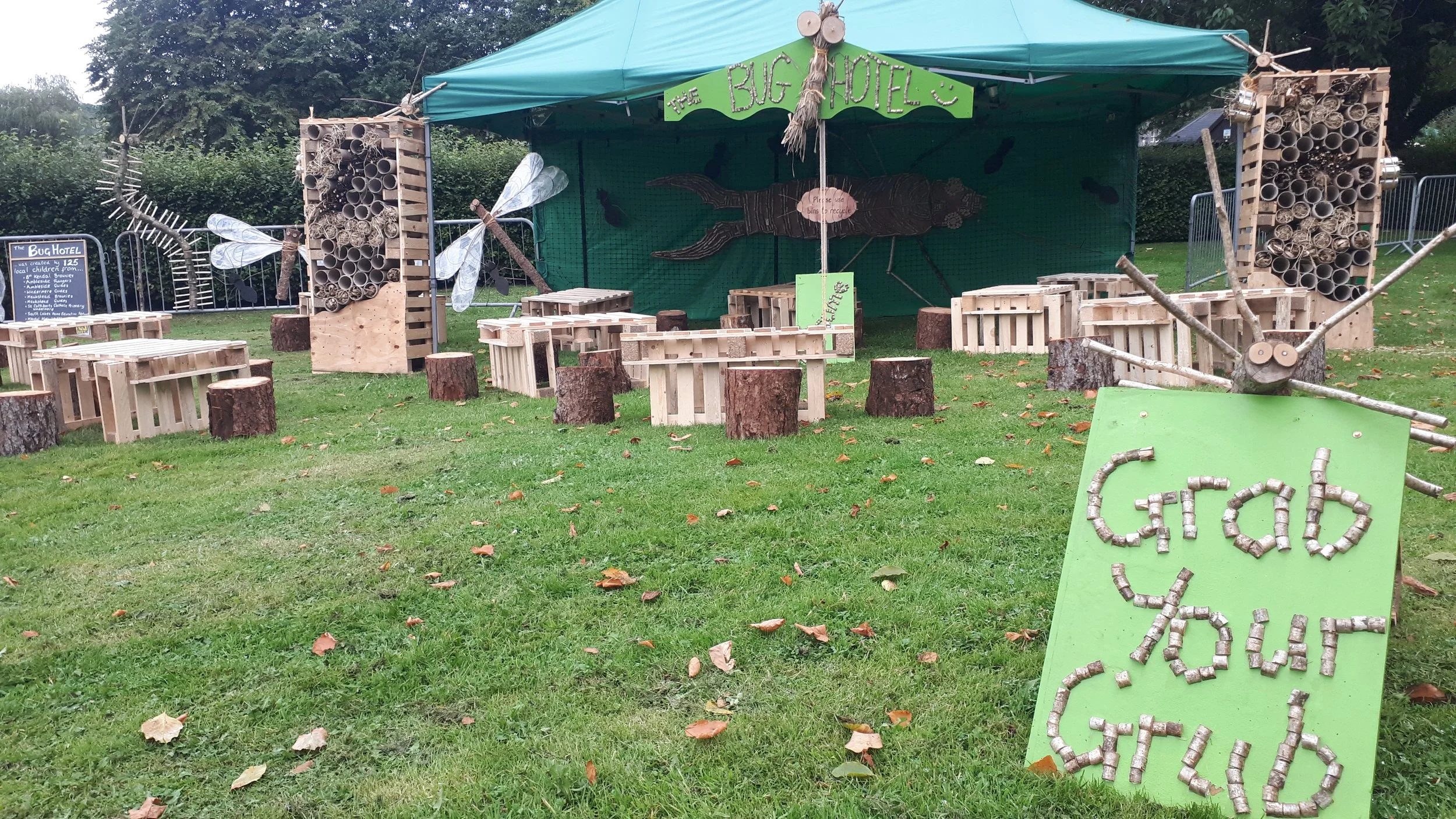 Outdoor craft area with a green tent labeled 'The Bug Hotel' and furniture made of wooden pallets and tree stumps, featuring insect-inspired decorations