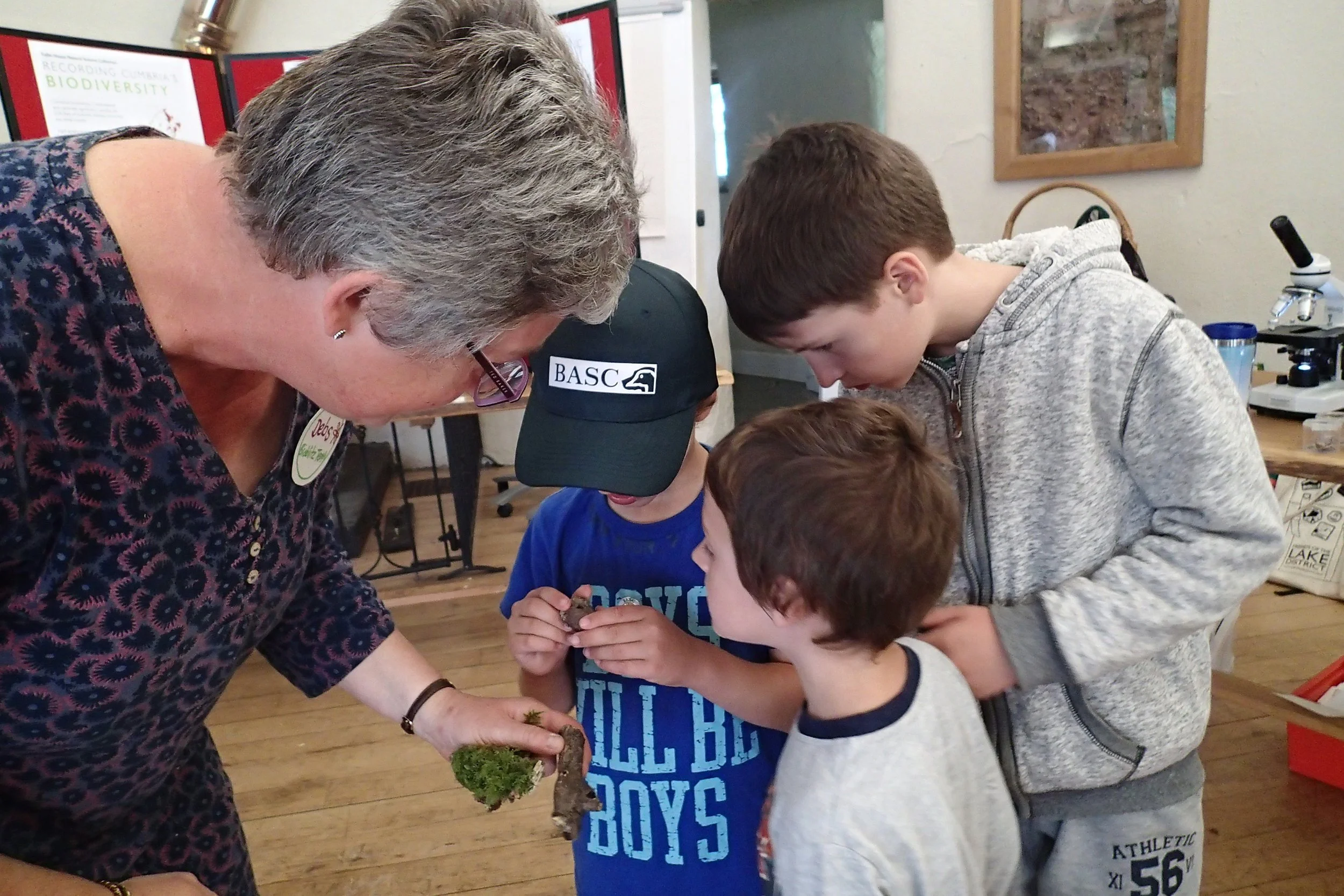 Adult woman showing four young boys natural specimens in a classroom or laboratory setting.