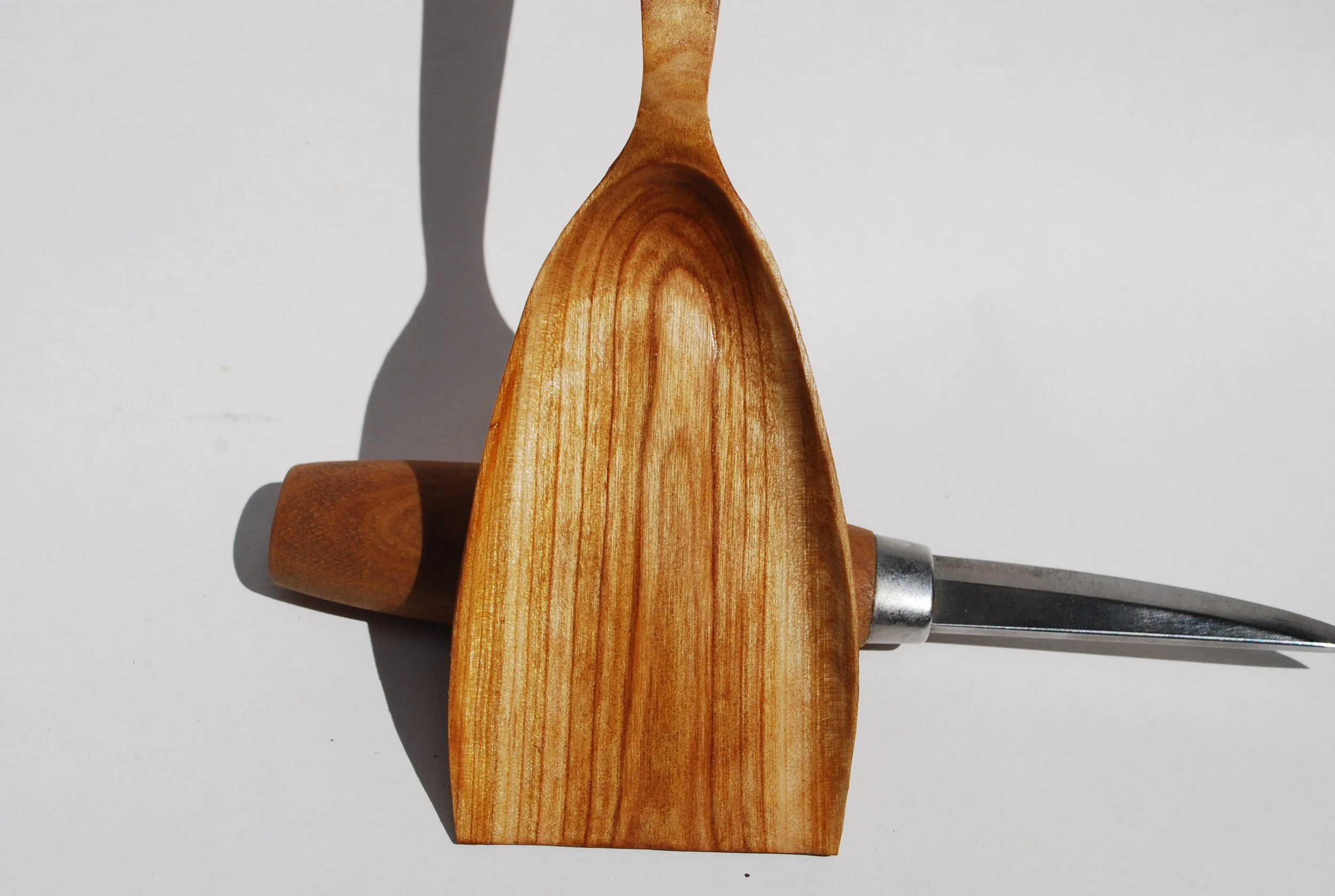 Wooden kitchen utensils - a spoon, a rolling pin, and a knife with a gray handle, arranged on a white background.