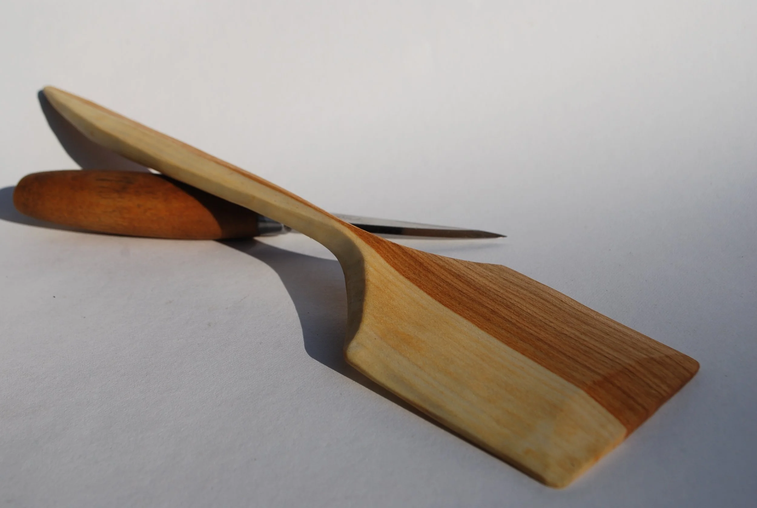A wooden spoon and a pebble placed on a white surface with a white background.