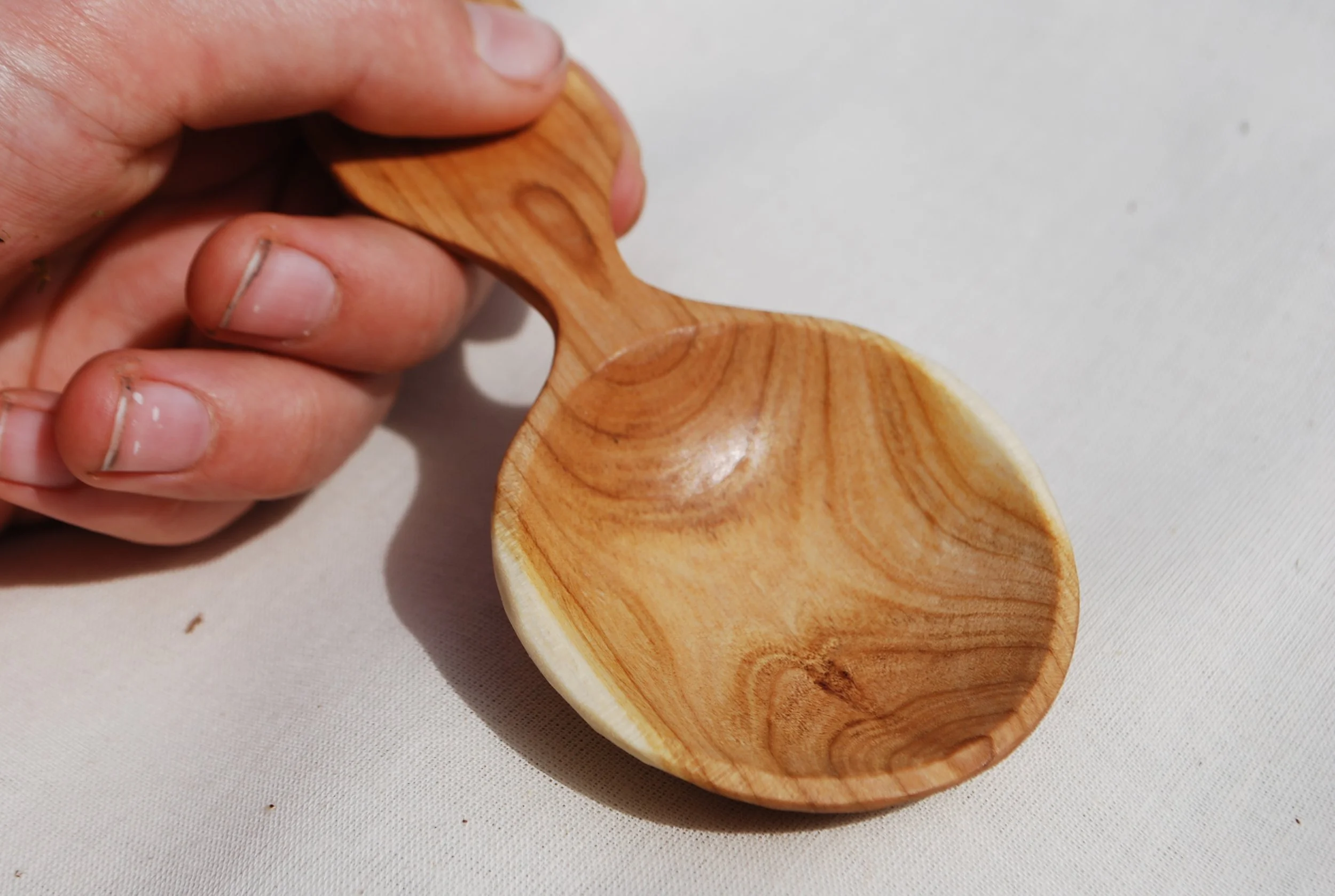 Hand holding a small wooden spoon over a white surface.