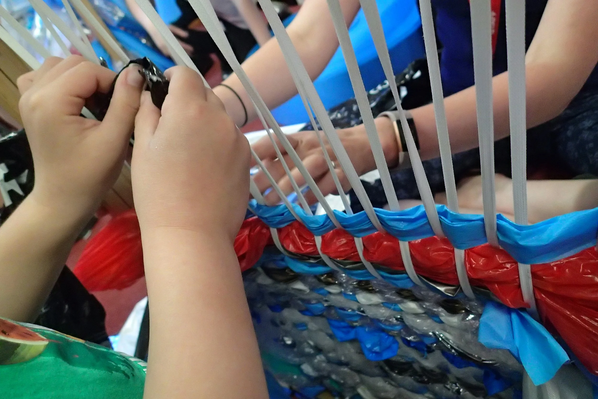 People weaving plastic bags into a makeshift fence or barrier.