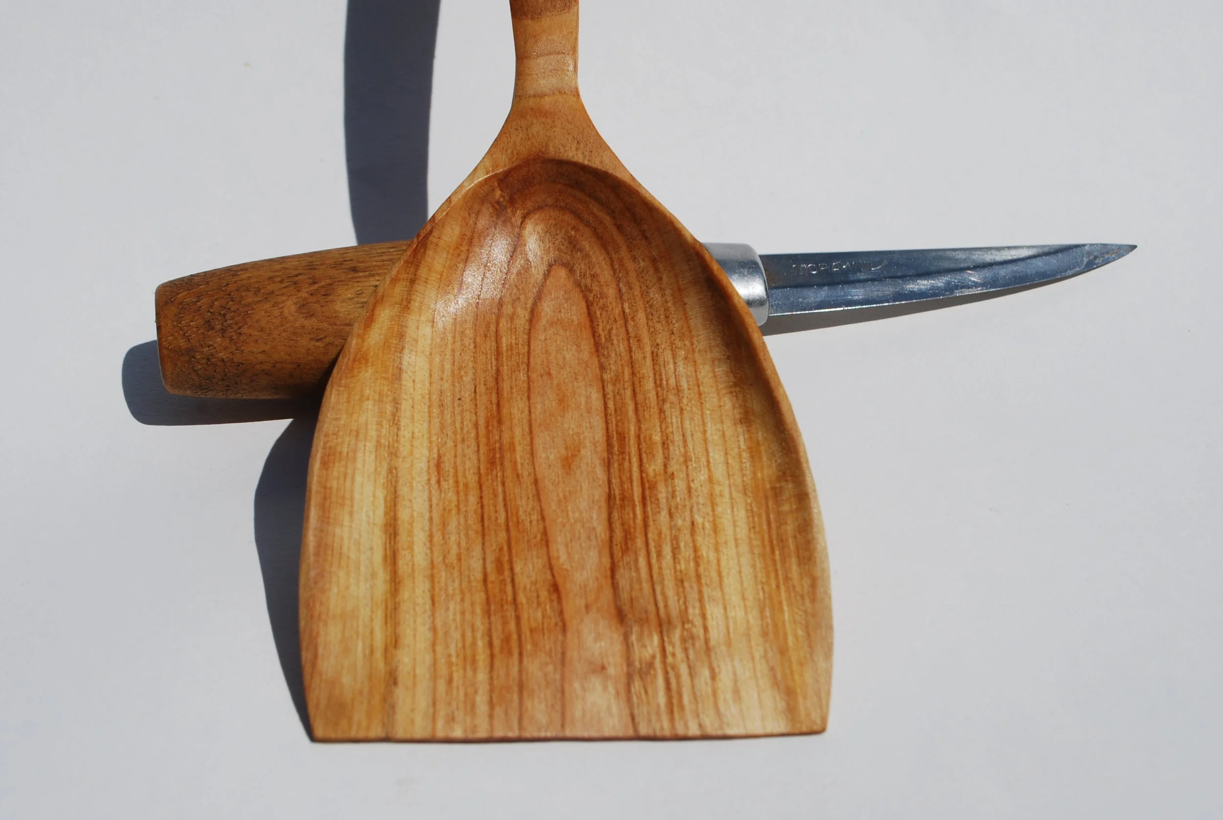 Wooden kitchen spatula, a wooden rolling pin, and a small knife on a white surface.