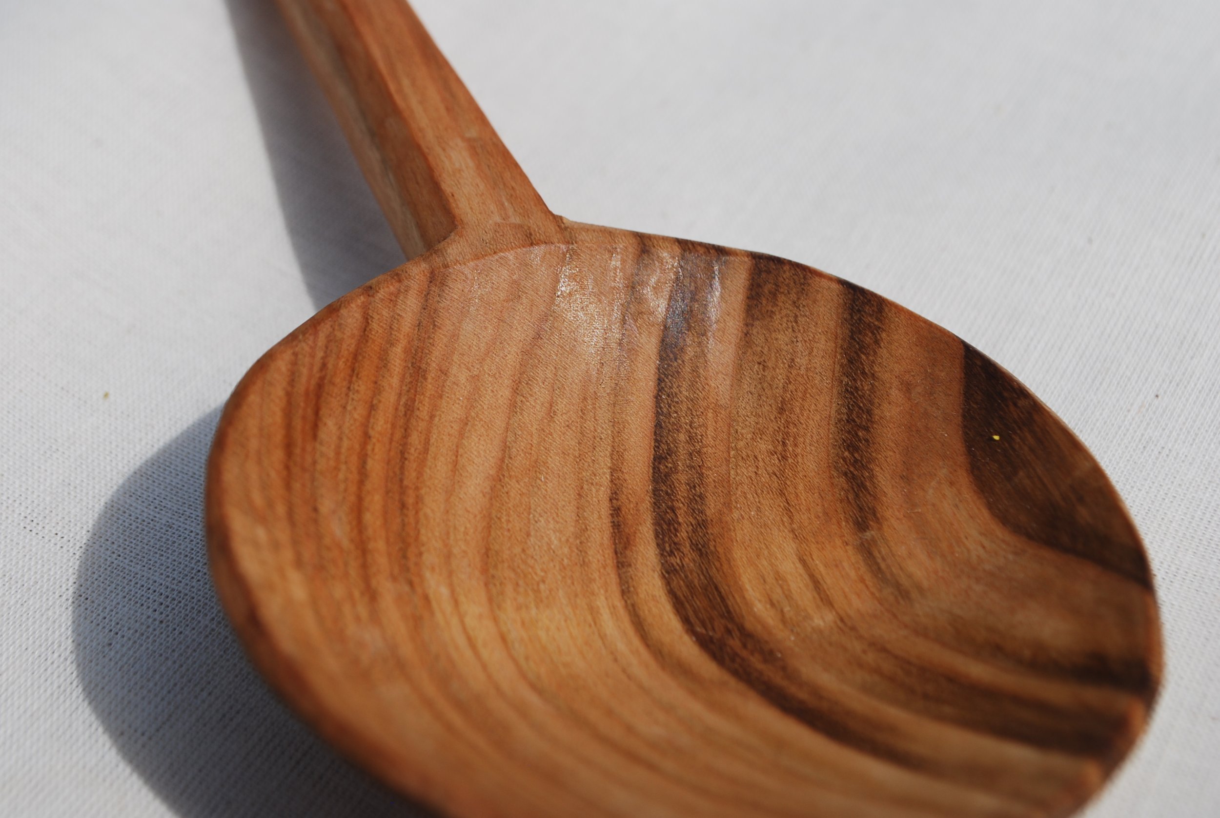 Close-up of a wooden spoon showing its smooth, polished surface with wood grain patterns, resting on a white surface.