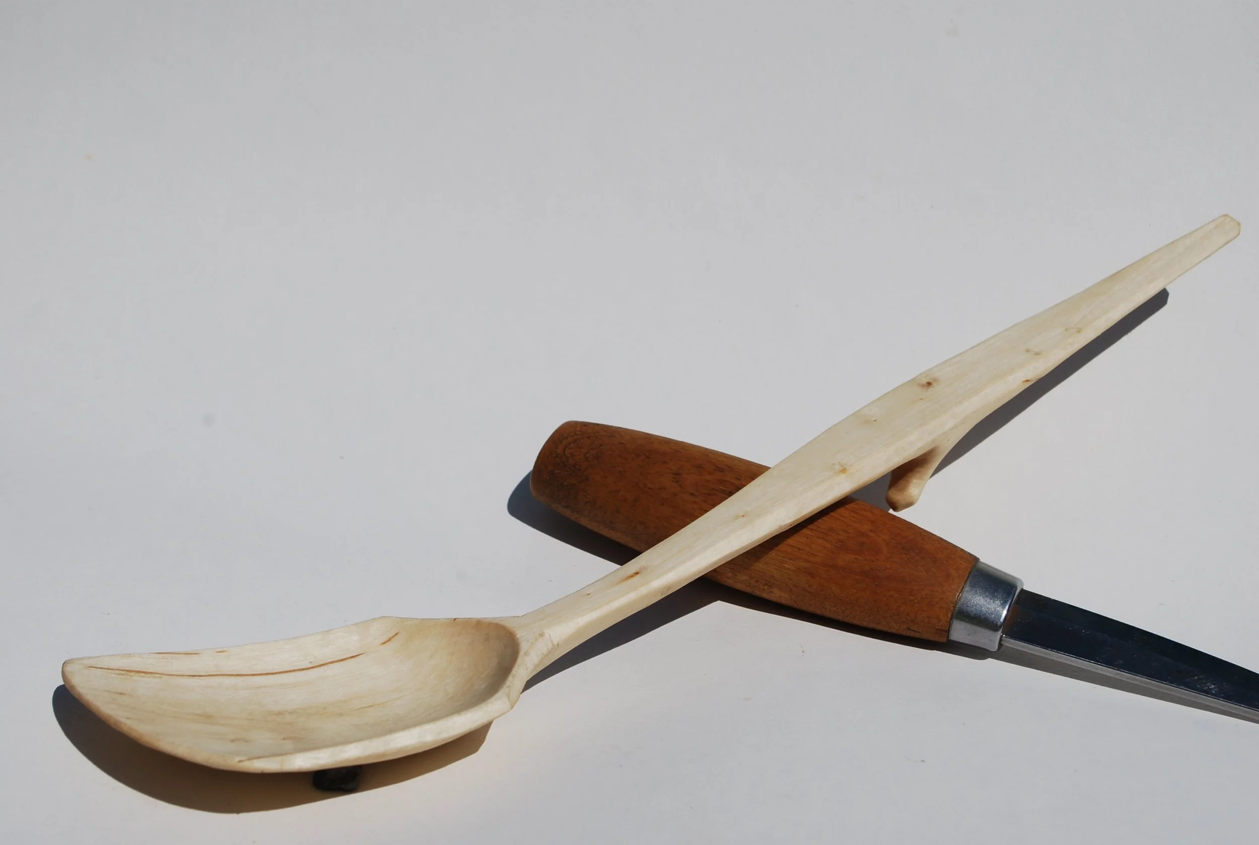 A wooden spoon, a carving knife, and a wooden spatula resting on a plain white surface.
