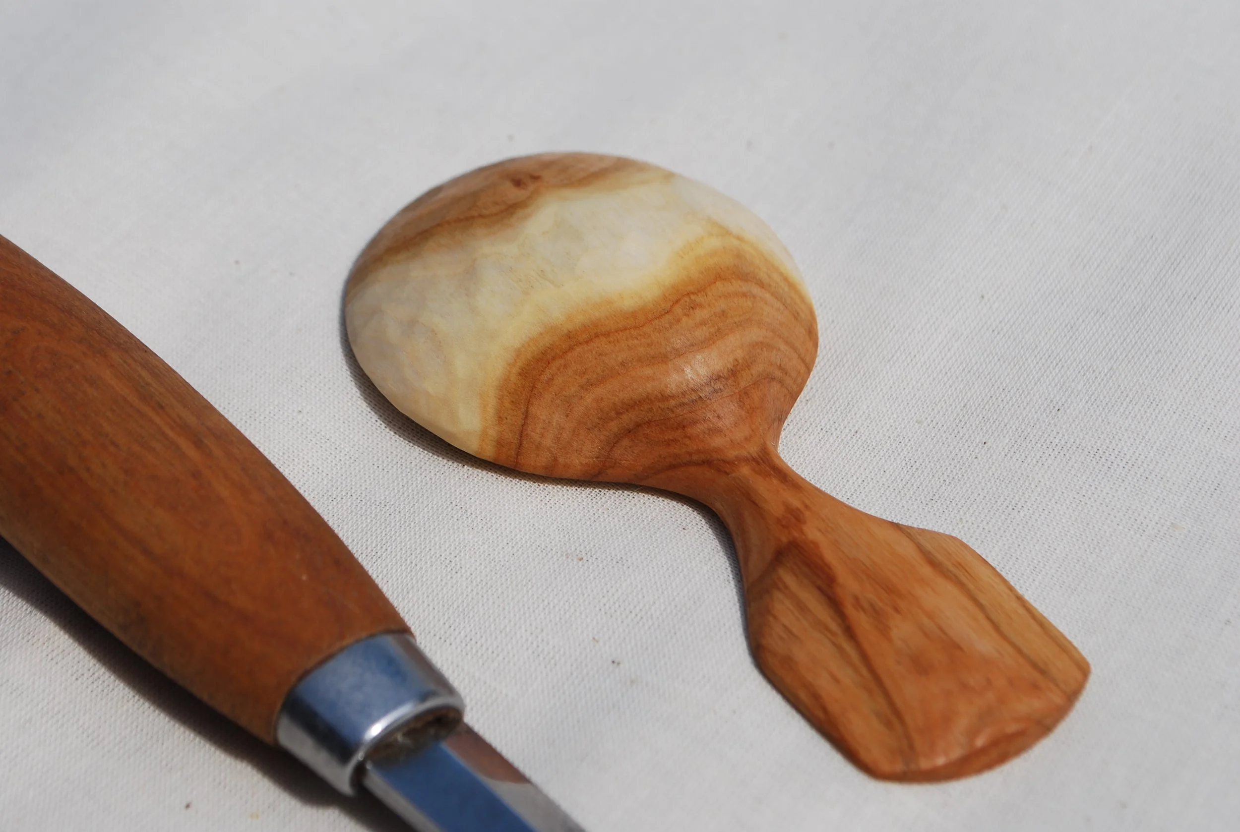 A handmade wooden massage roller with a smooth, rounded stone attached, lying on a white fabric surface.