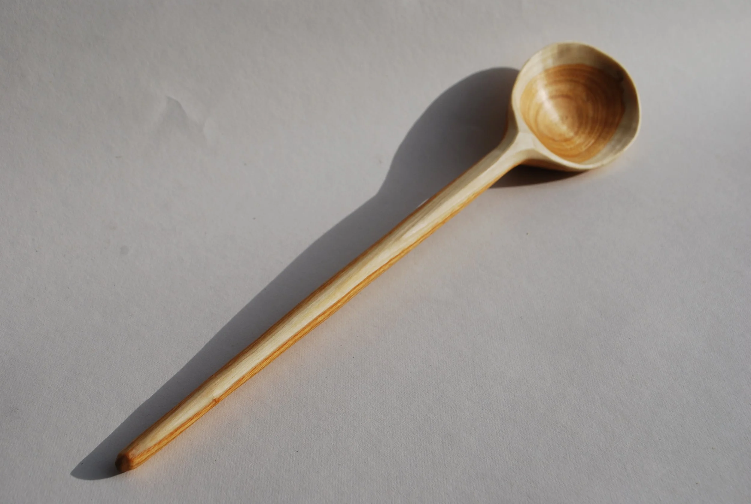 Wooden ladle with a round bowl and long handle lying on a white surface.