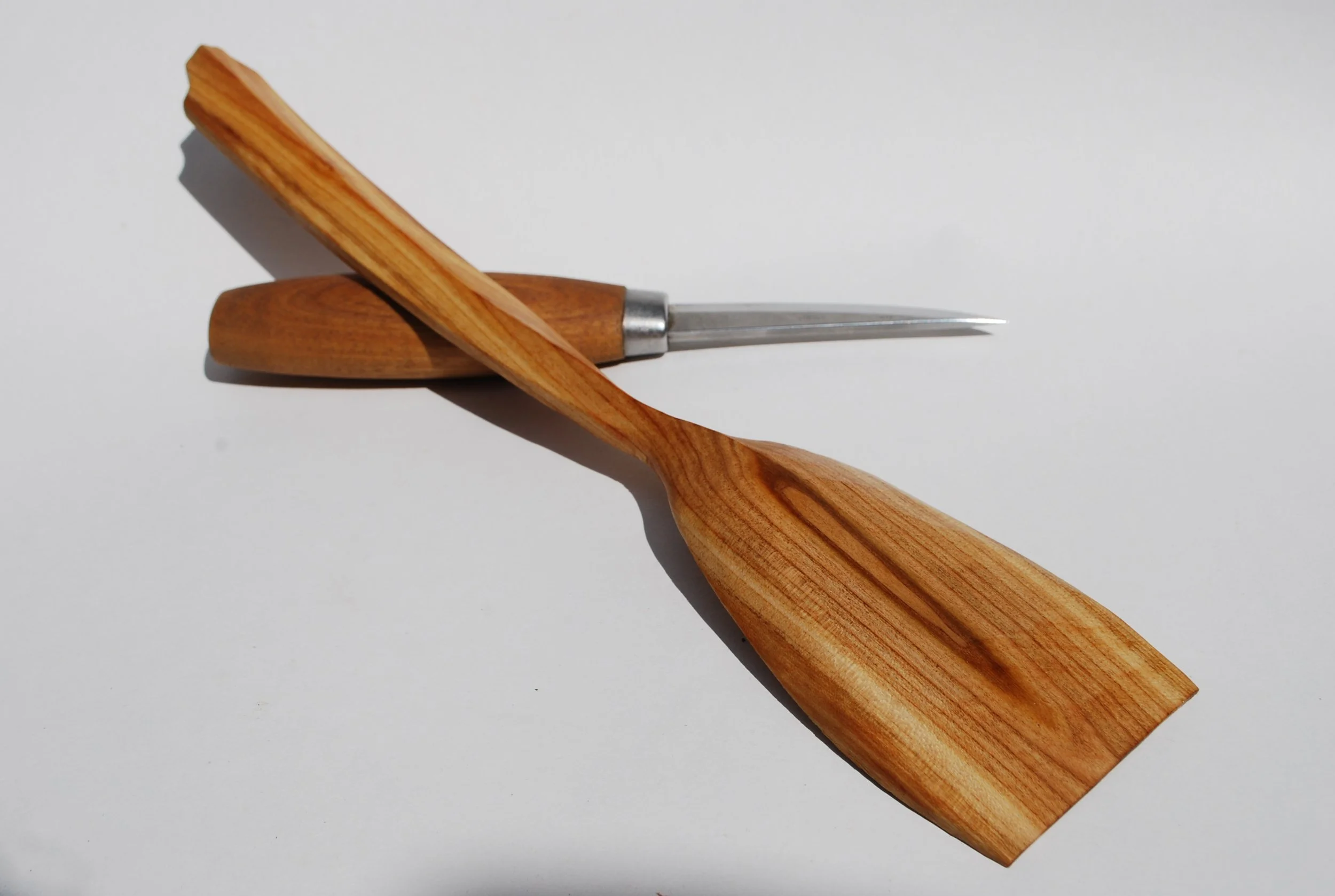 A wooden spatula and a carving knife with a wooden handle, arranged on a white surface.