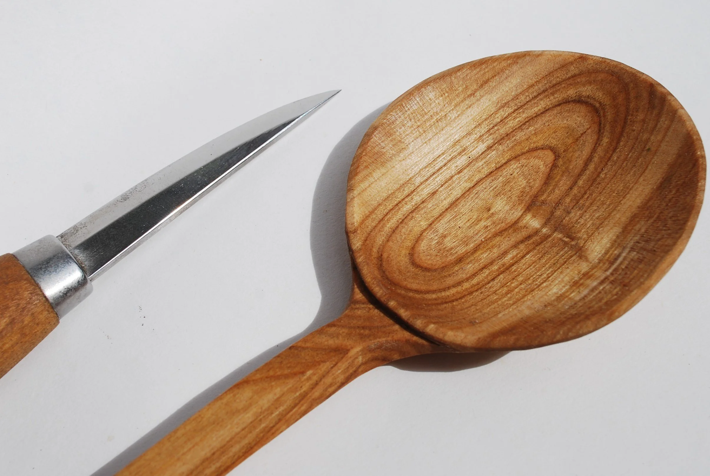 A wooden spoon and a metal knife with a wooden handle on a white surface.