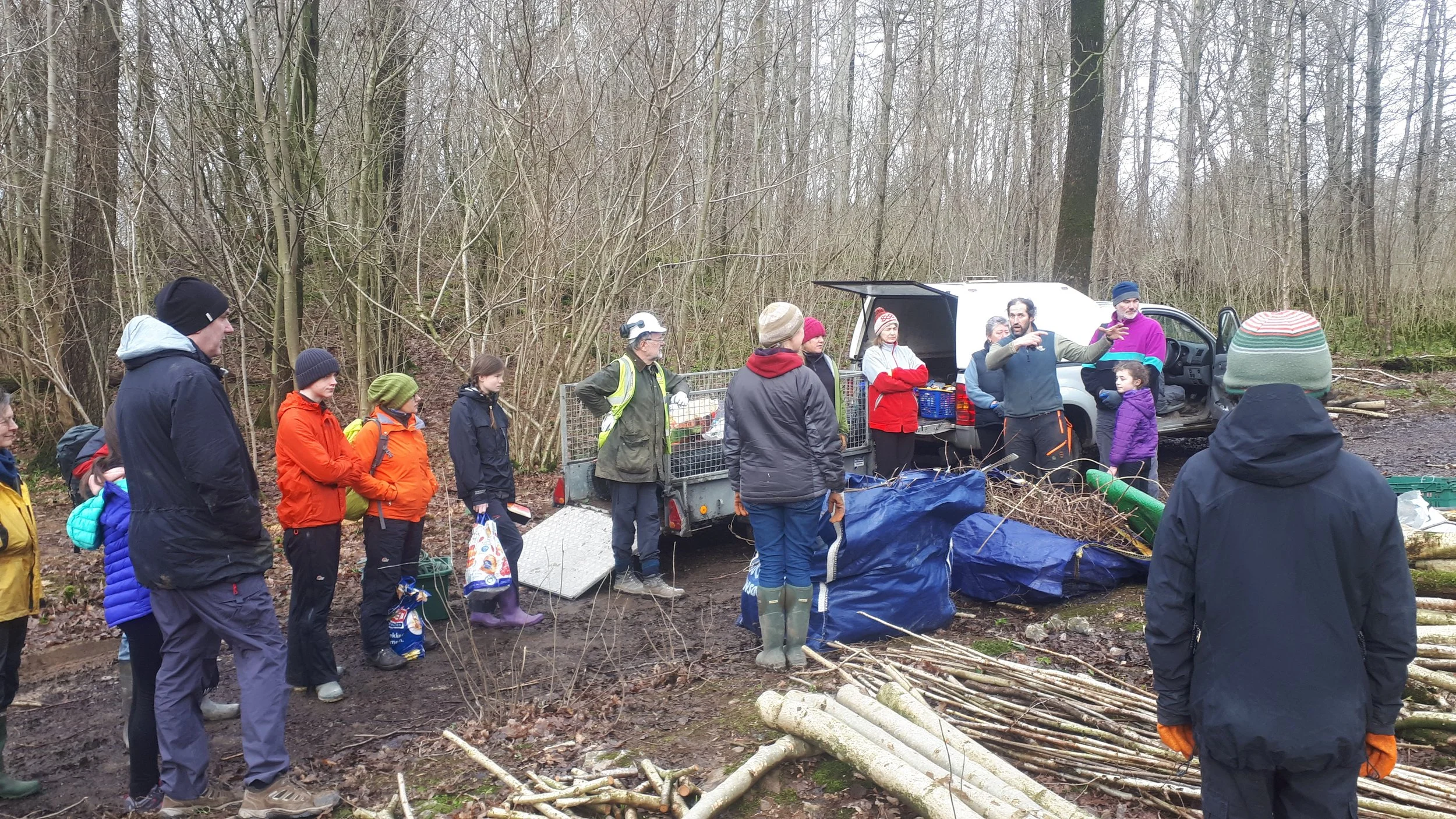 Group of people gathered outdoors in a wooded area, some wearing rain gear, participating in a conservation activity 